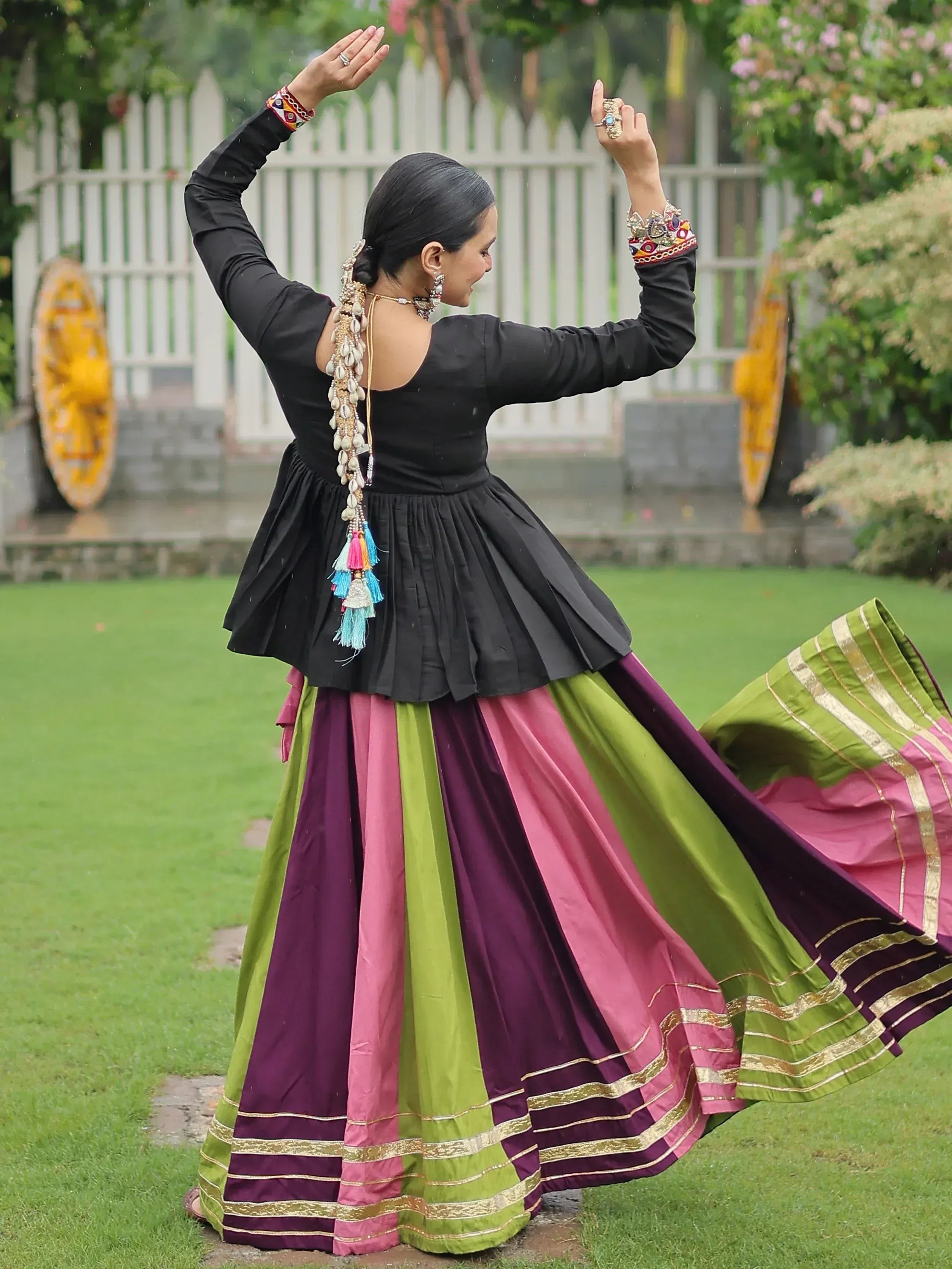 Woman in black top and colorful striped lehenga dancing outdoors