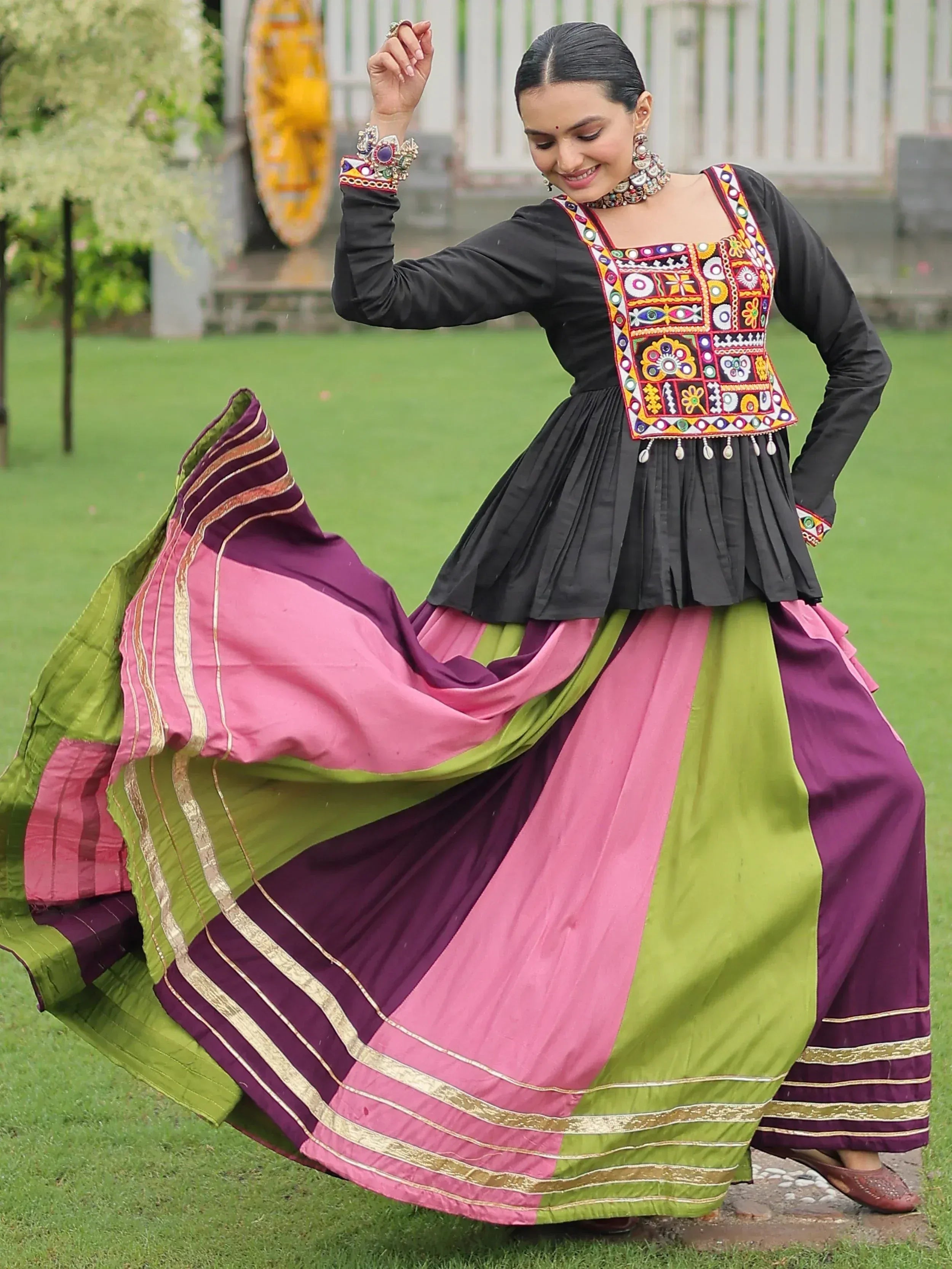 Woman in black embroidered top with colorful patchwork and vibrant pink, green, purple skirt, dancing outdoors