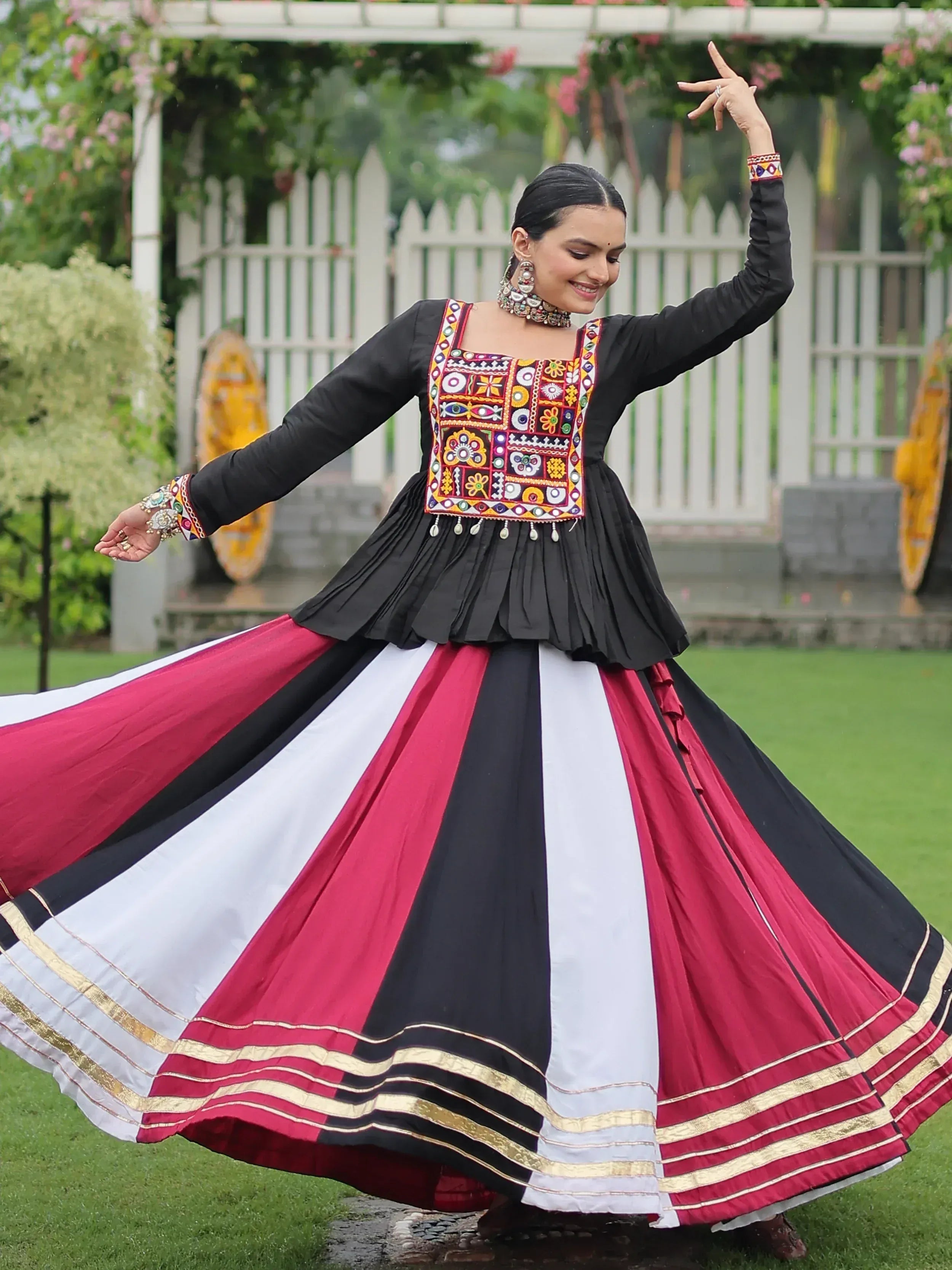 Woman in black, red, white ethnic gown with mirror work, dancing outdoors