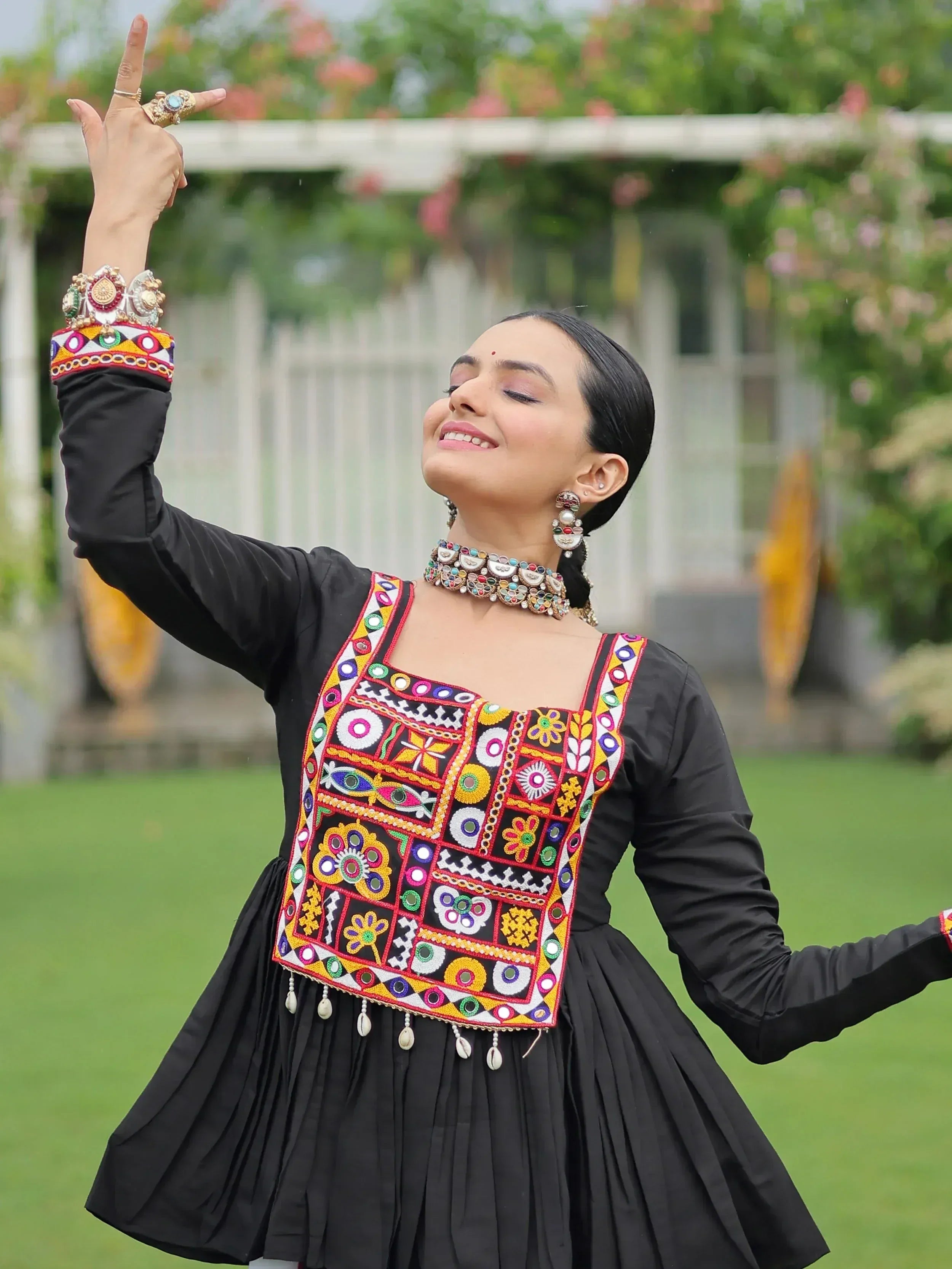 Woman in black ethnic gown with colorful mirror embroidery, dancing outdoors