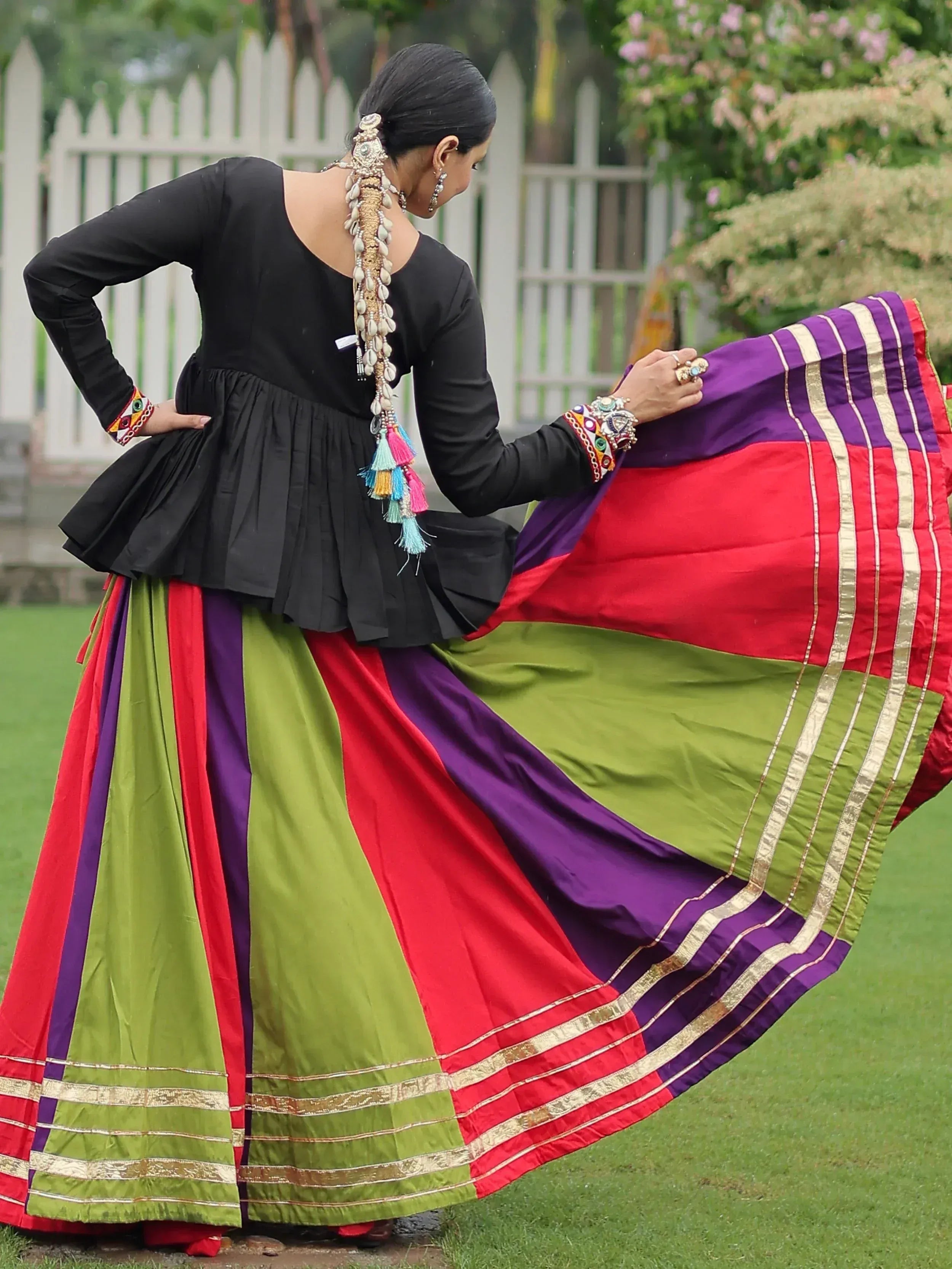 Woman in colorful Indian ethnic wear with black top, multicolor skirt, and traditional jewelry outdoors