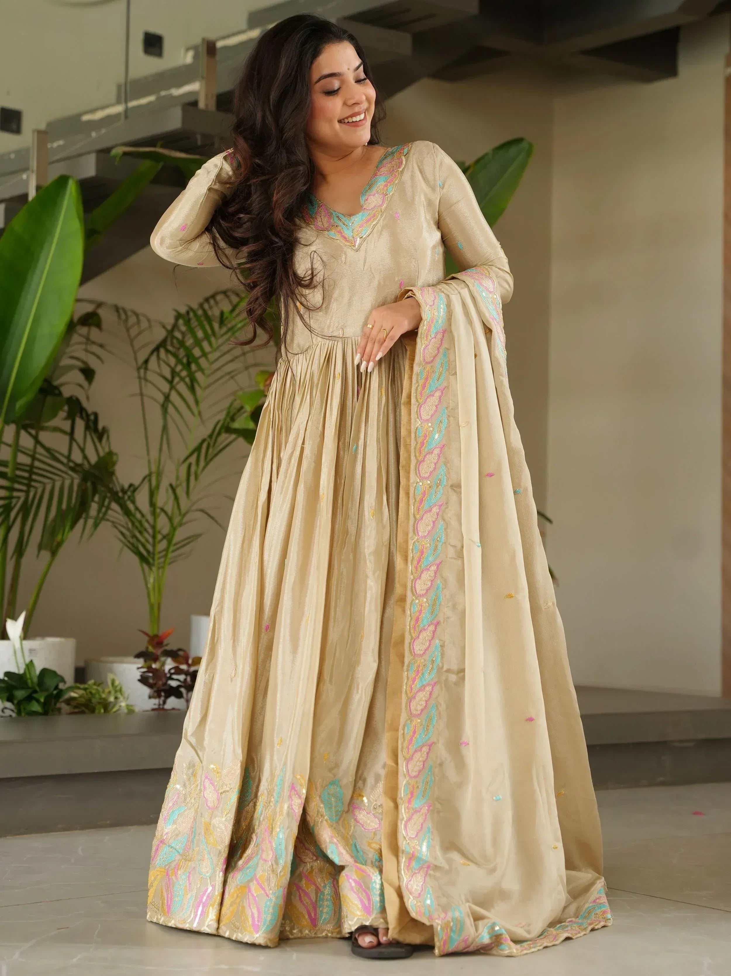 Beige embroidered ethnic gown with colorful floral detailing, perfect for Indian festive occasions