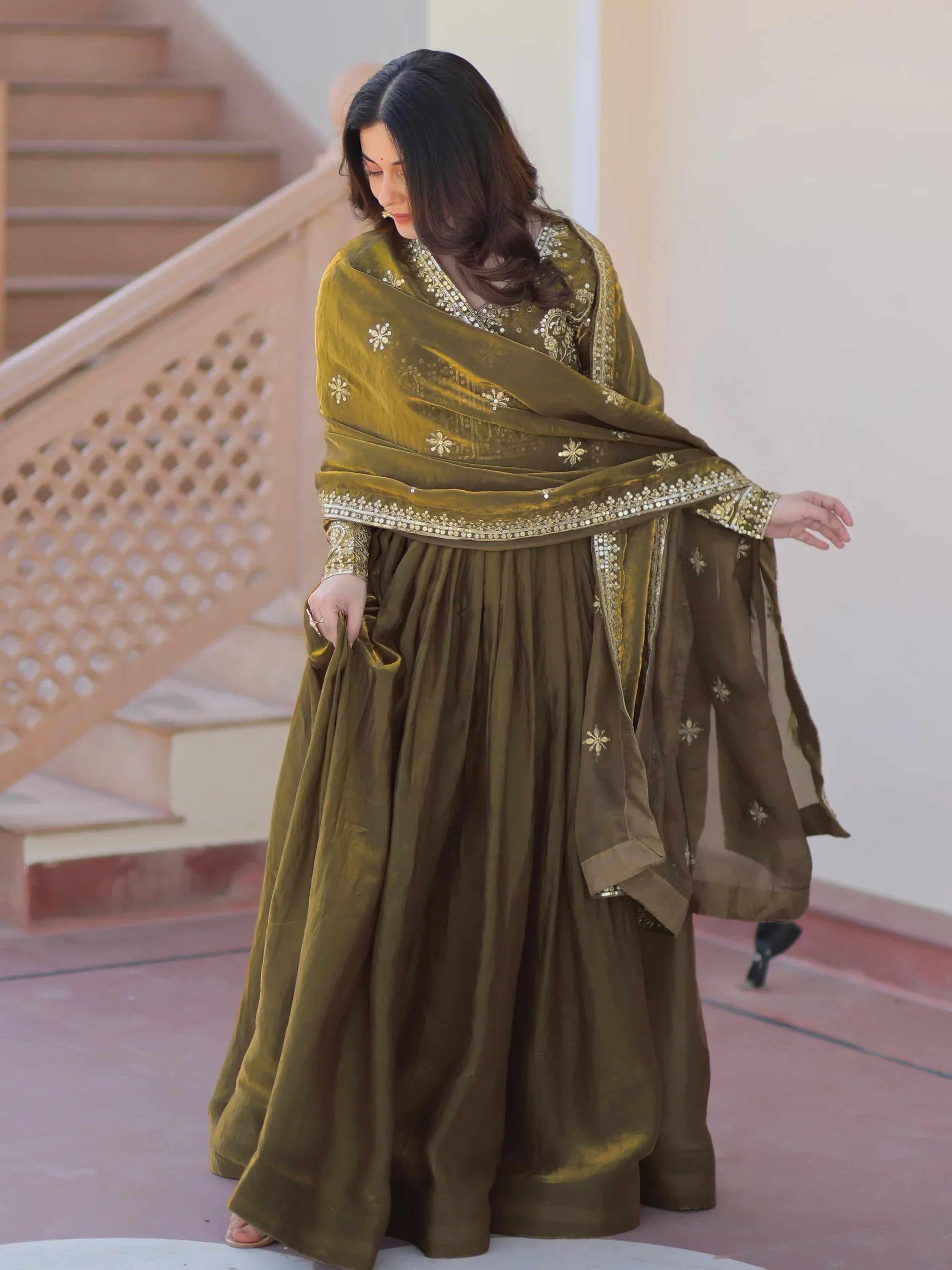 Woman wearing olive green embroidered ethnic gown with dupatta, outdoor setting