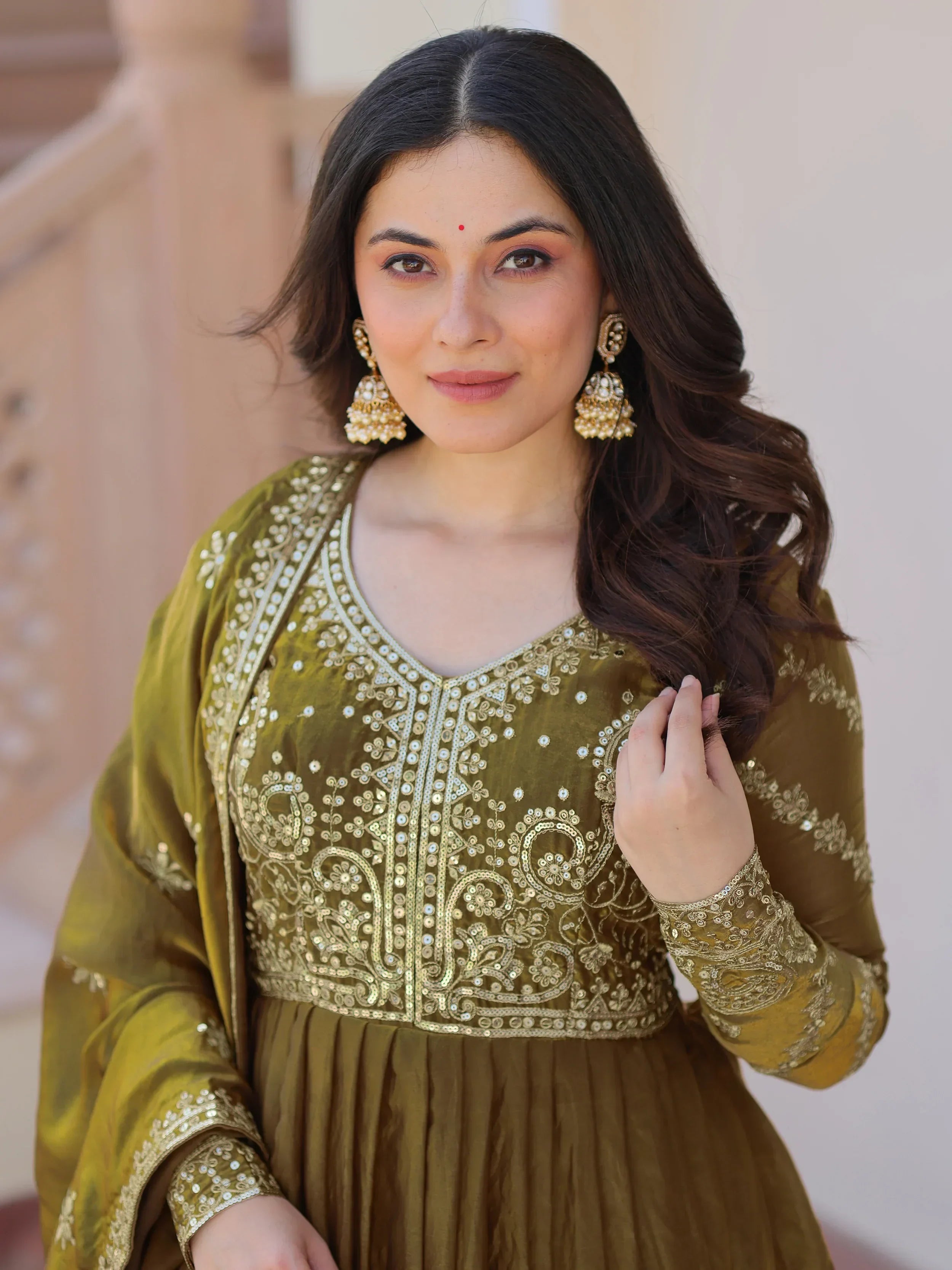 Woman wearing olive green embroidered Anarkali suit with gold details and statement earrings