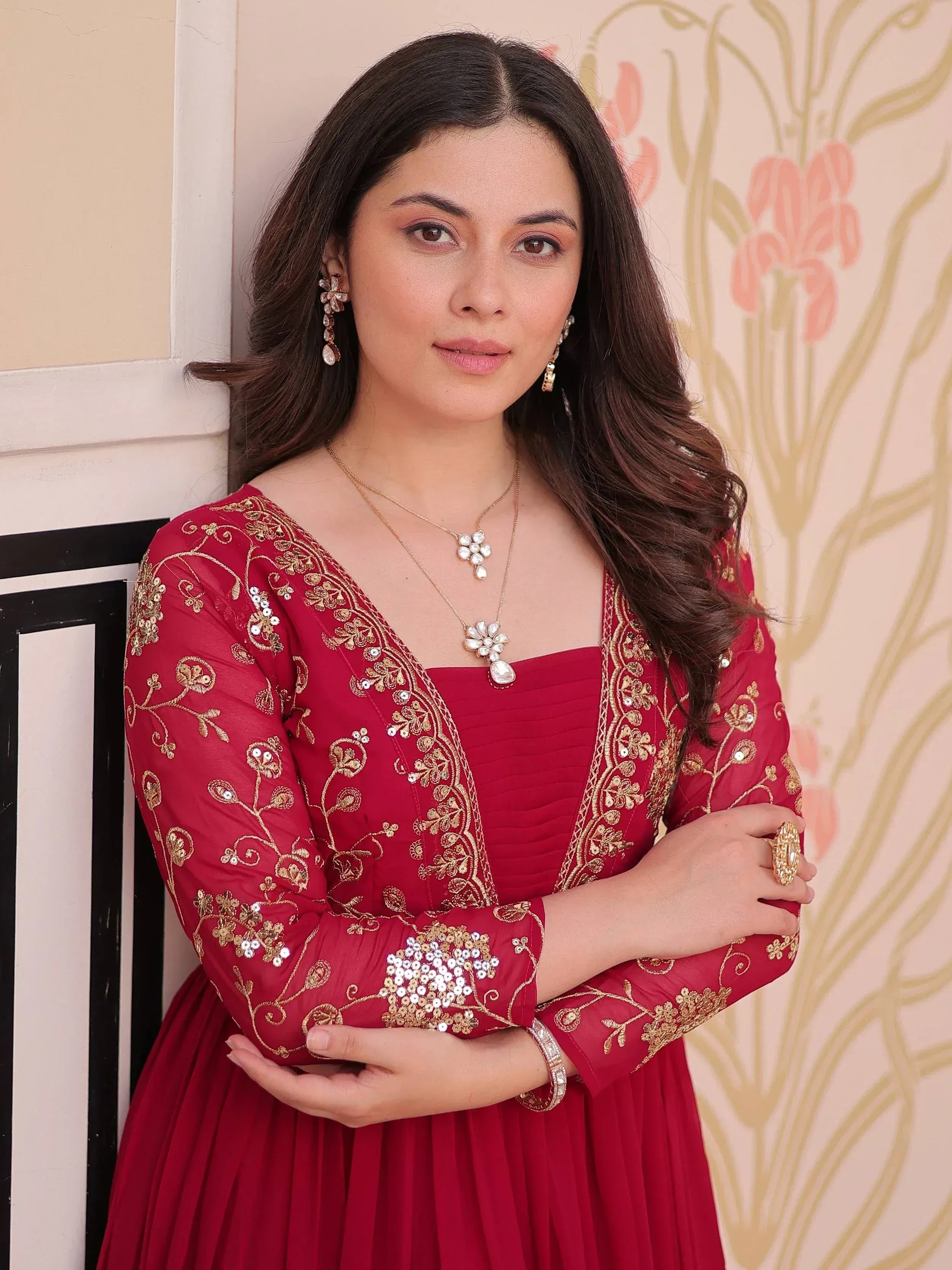 Woman in red ethnic gown with gold embroidery and sequins, styled with floral jewelry for festive occasions