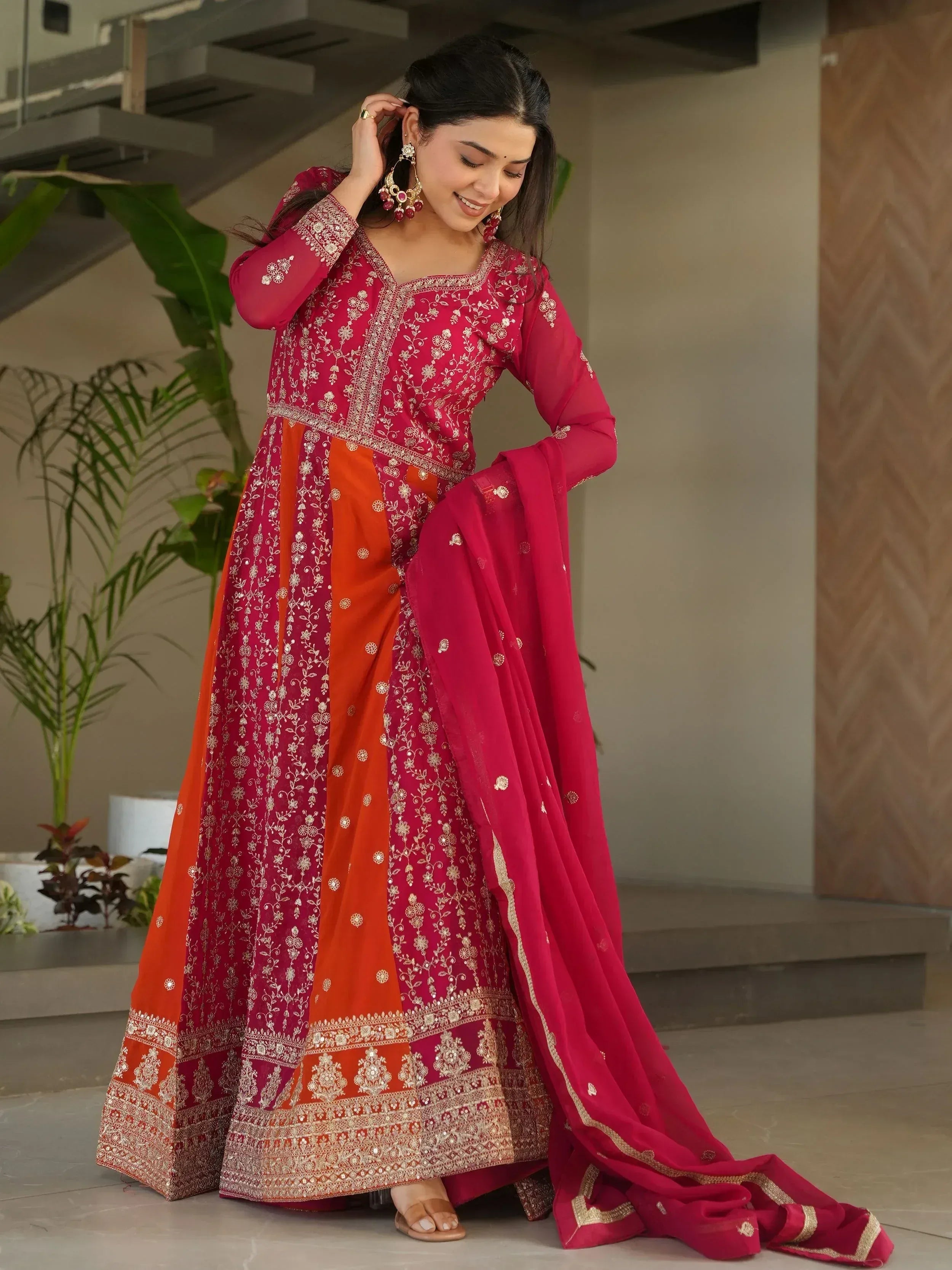 Woman in red and orange embroidered Indian ethnic anarkali suit with gold detailing, perfect for weddings or festivals.