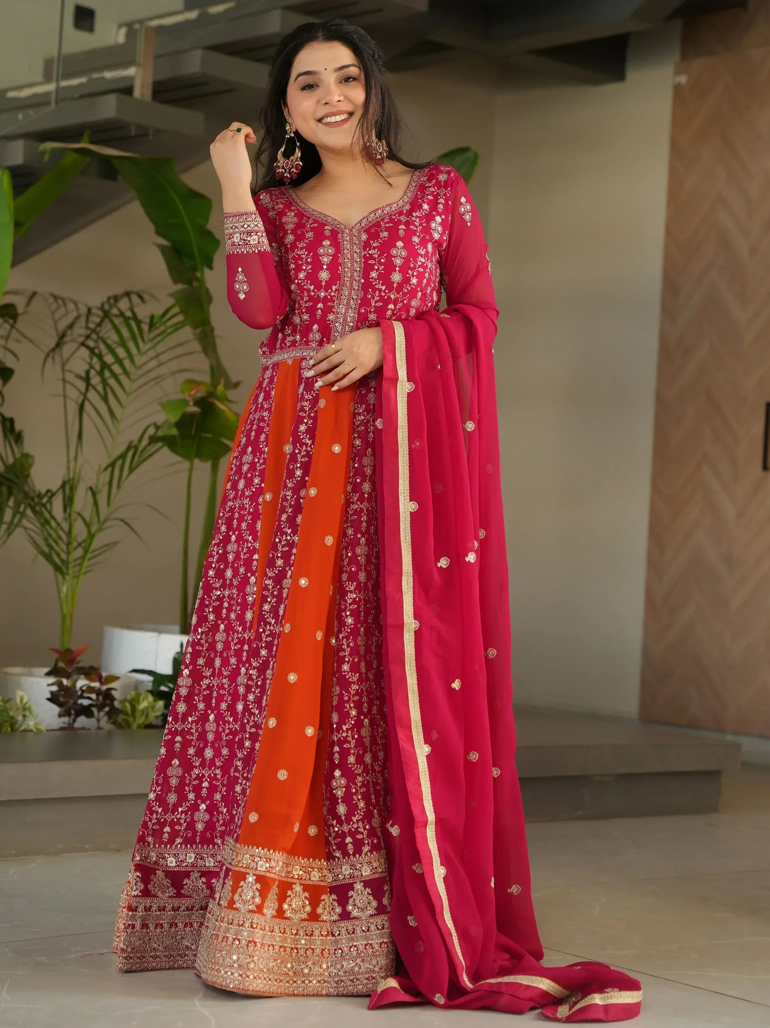 Woman in vibrant pink and orange embroidered Indian ethnic wear, perfect for festive occasions.