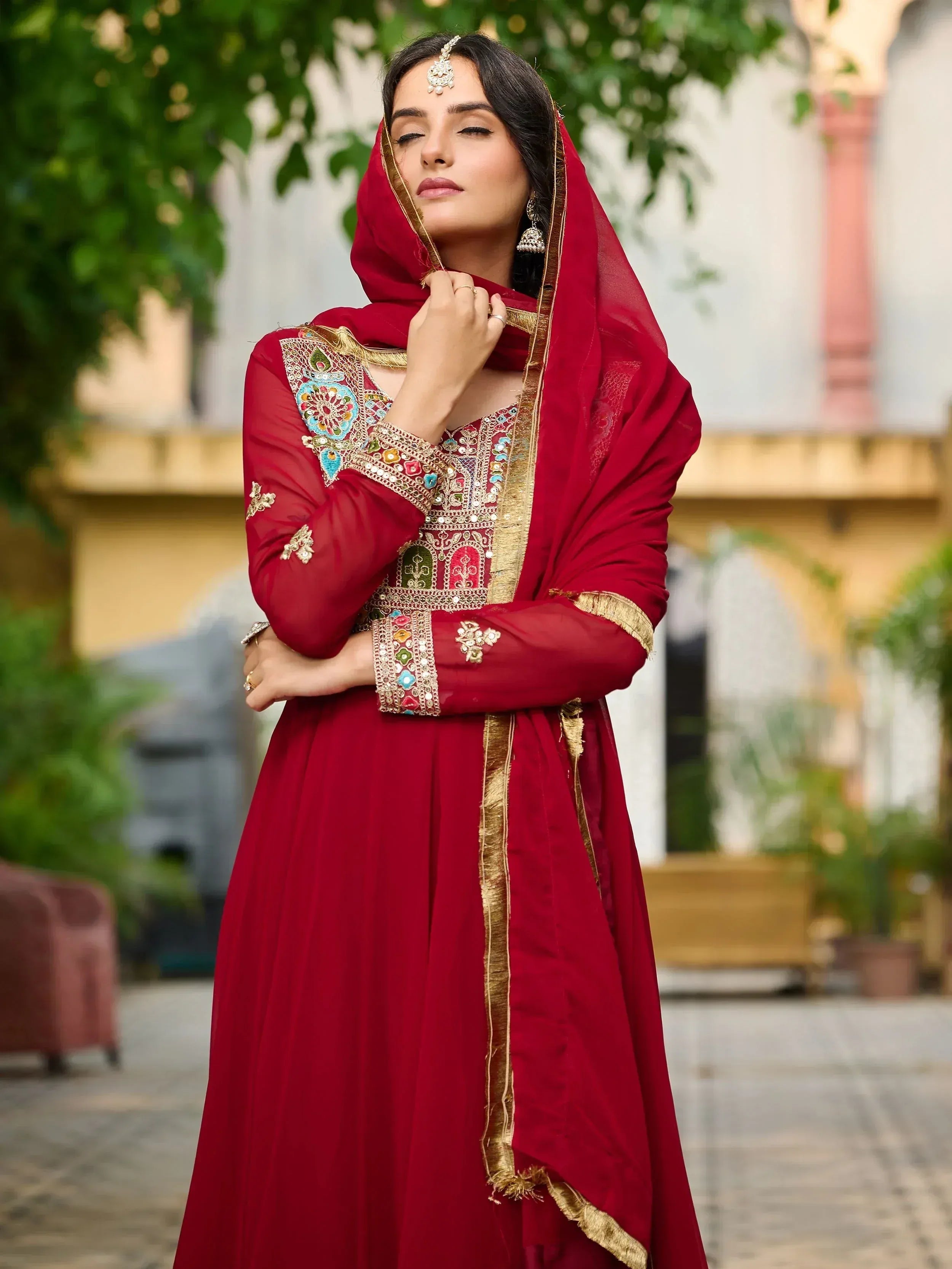 Elegant red ethnic gown with gold embroidery and colorful embellishments, perfect for festive occasions.