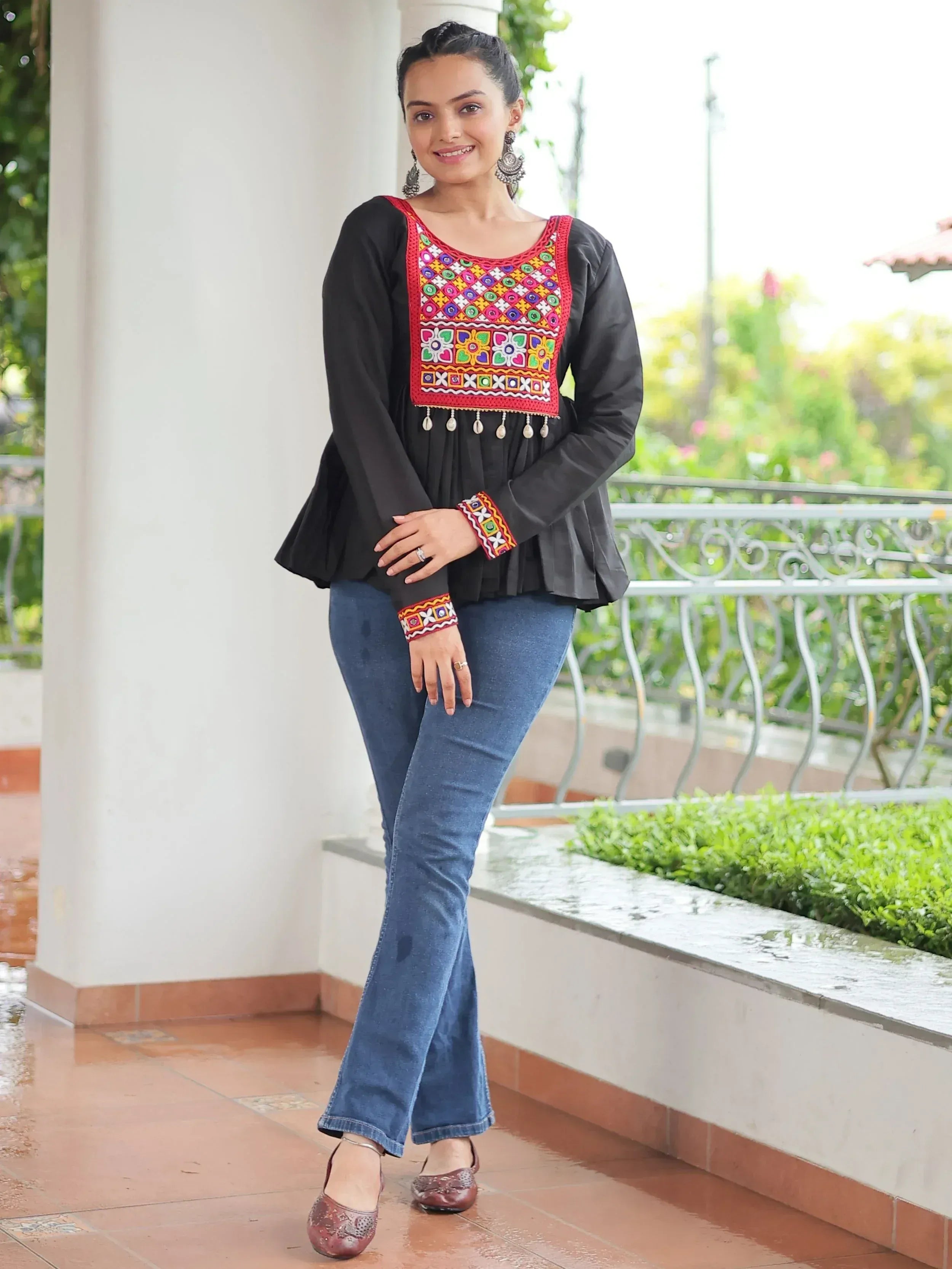 Black embroidered top with colorful mirror work, paired with blue flared jeans and ethnic jewelry for casual ethnic wear