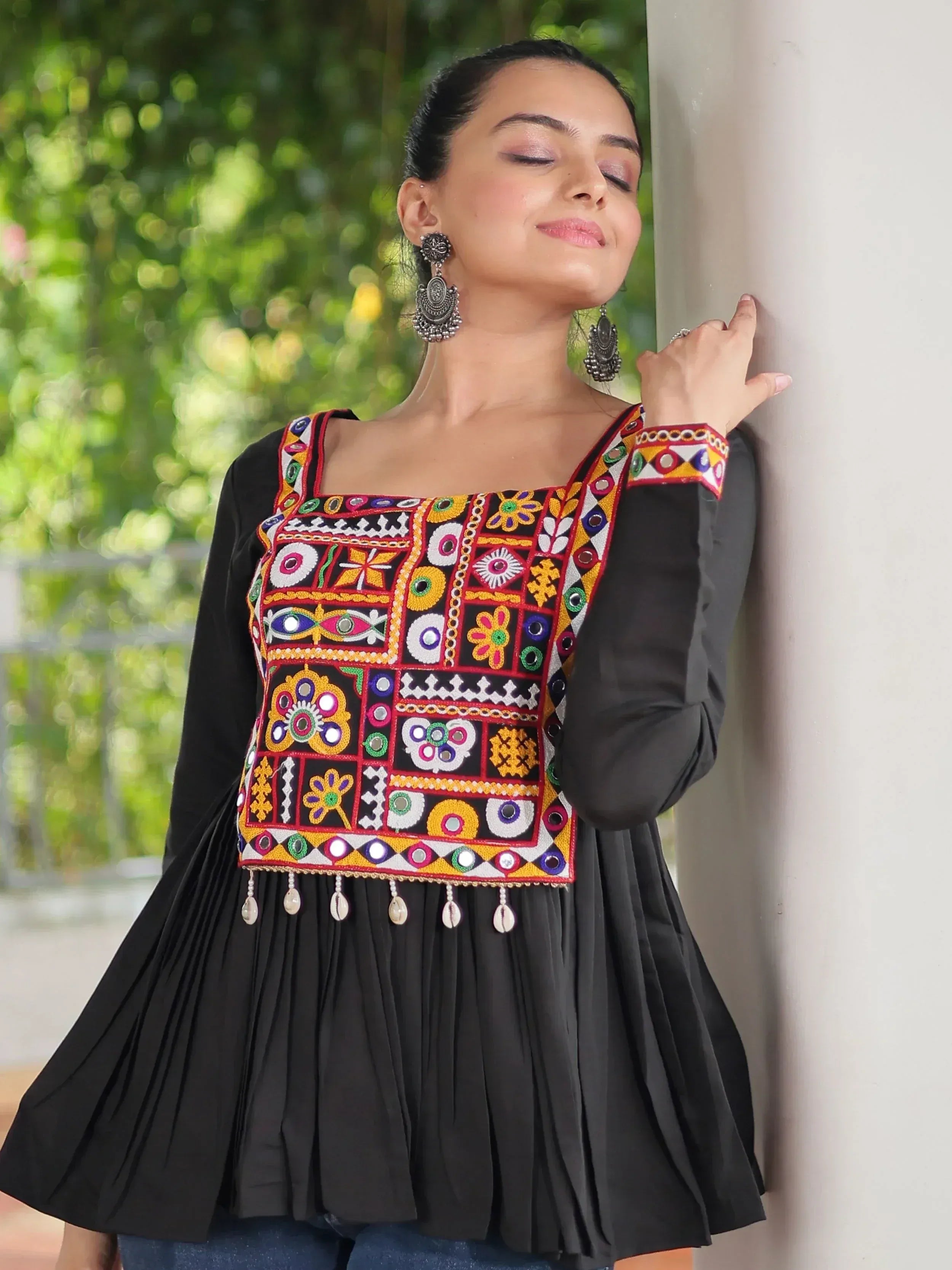 Black ethnic top with colorful mirror embroidery and pleated hem, paired with statement earrings.
