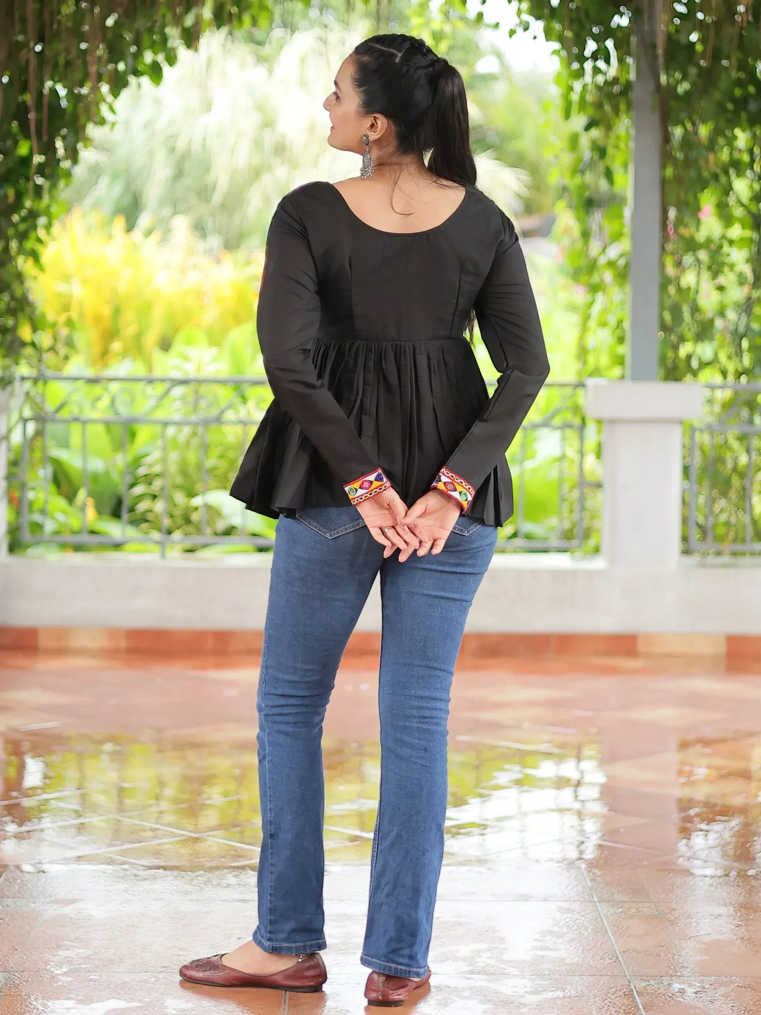 Black ethnic peplum top with colorful embroidery cuffs, paired with blue jeans and flats, garden backdrop