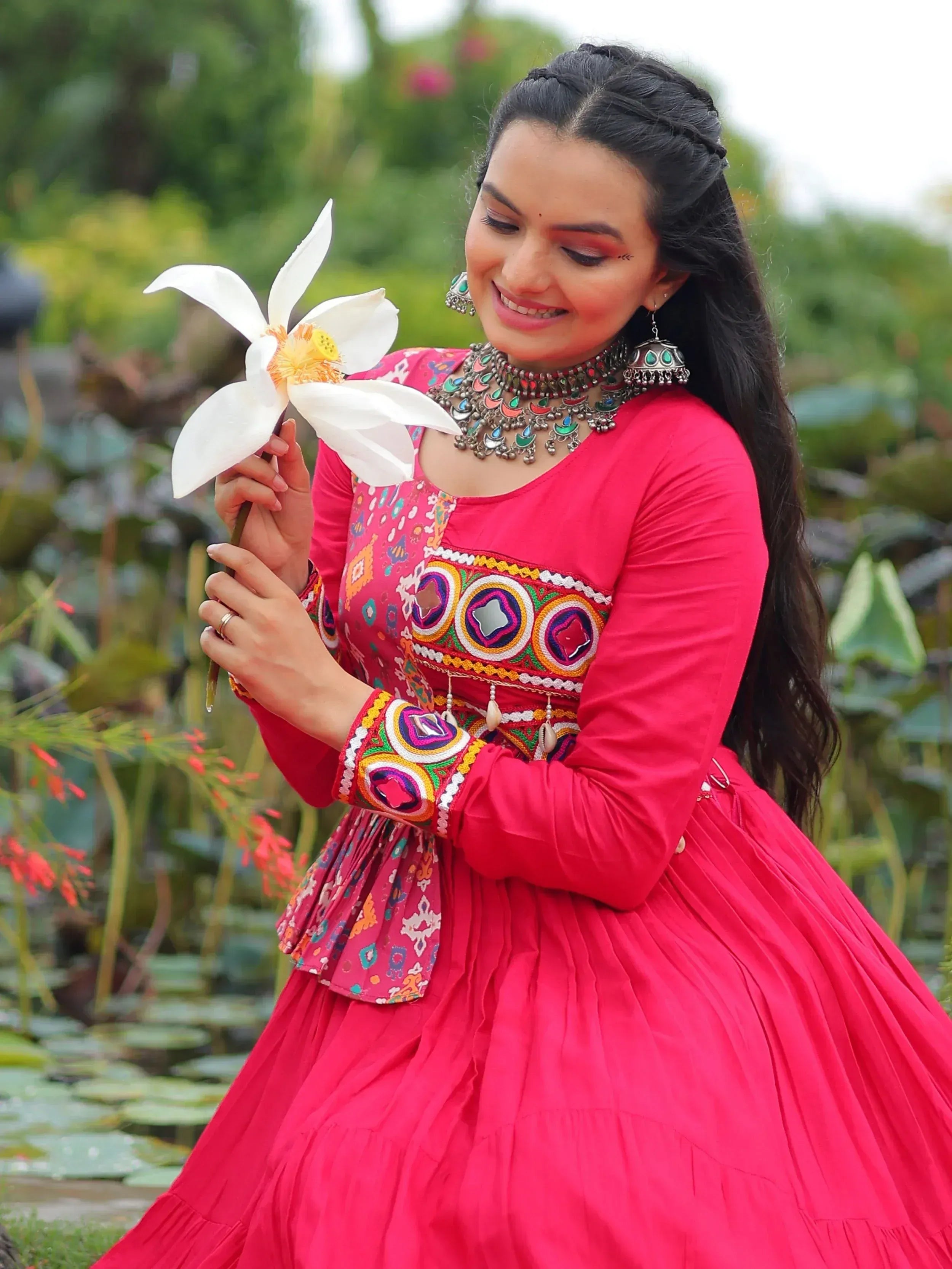 Woman in vibrant pink embroidered ethnic gown holding white lotus, traditional Indian wear