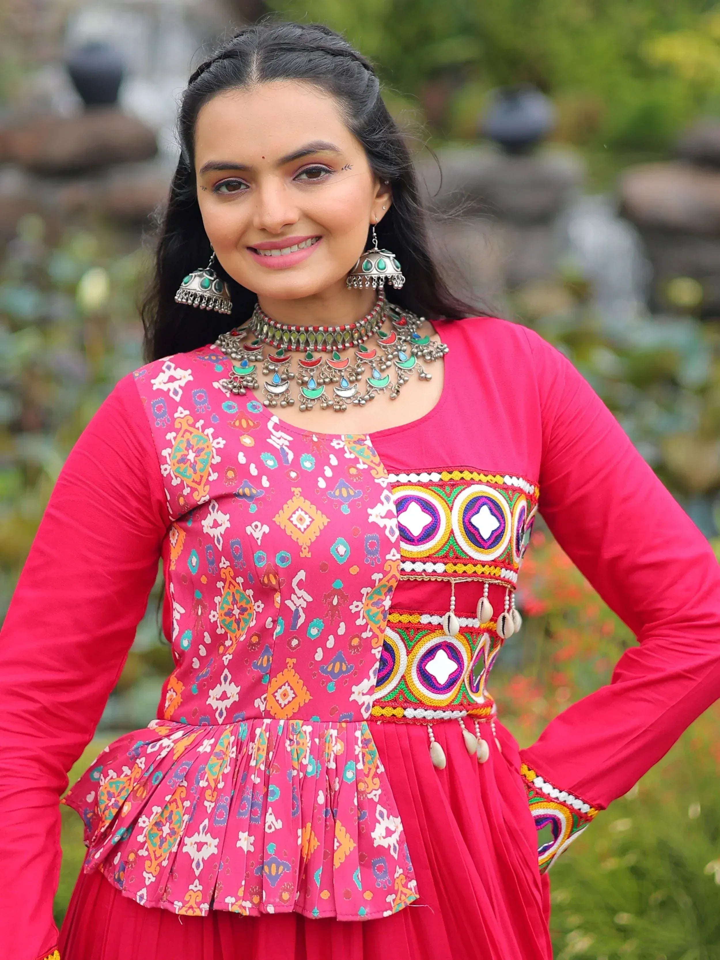 Woman in vibrant pink ethnic gown with colorful embroidery and traditional jewelry, perfect for festive occasions.
