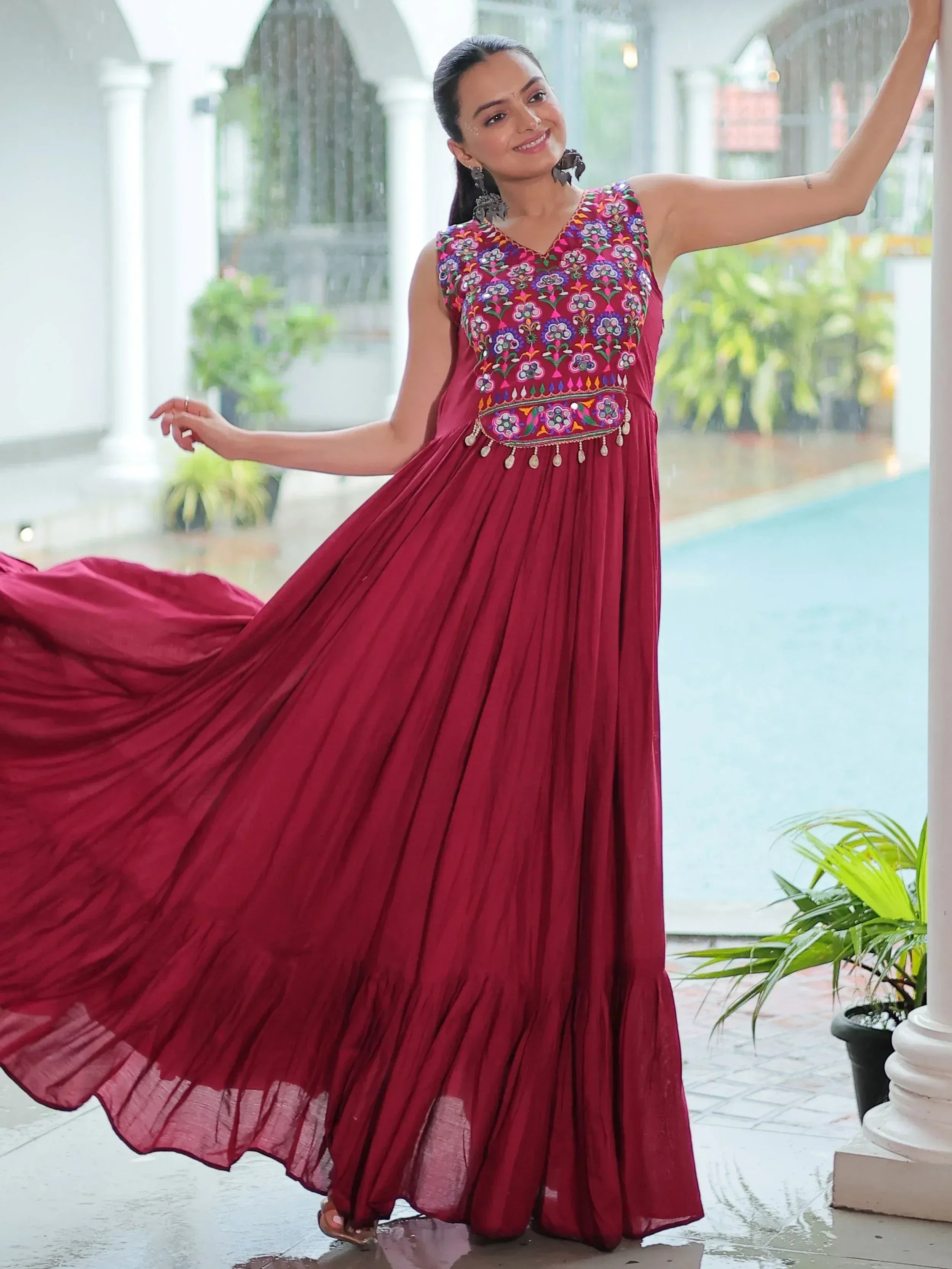 Woman in maroon ethnic gown with floral embroidery, pleated skirt, dancing near poolside