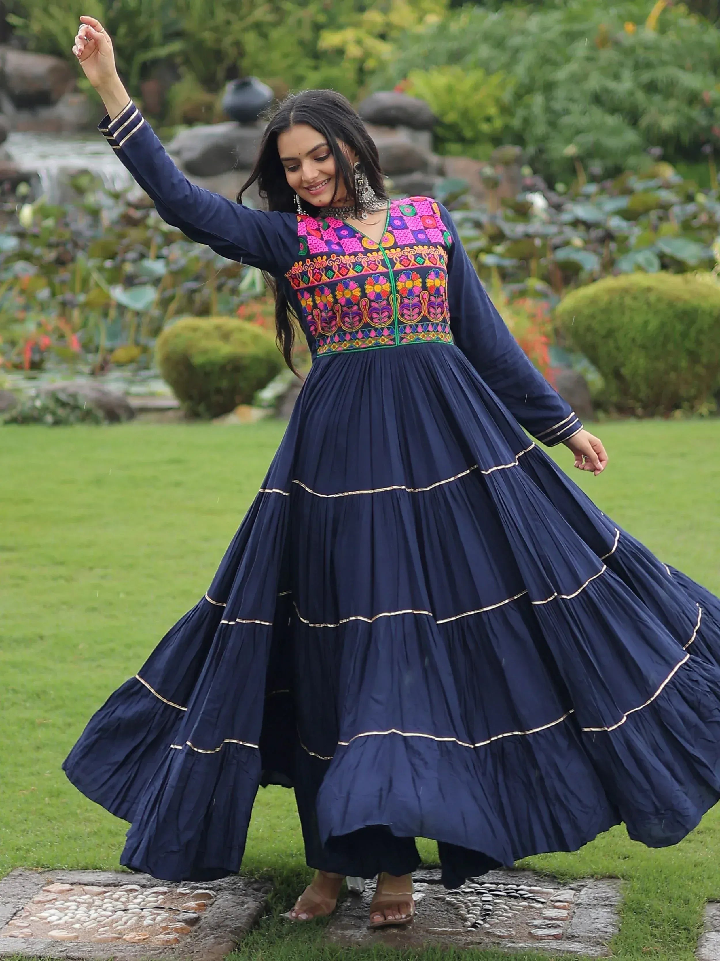 Woman in navy blue ethnic gown with vibrant floral embroidery, twirling in garden