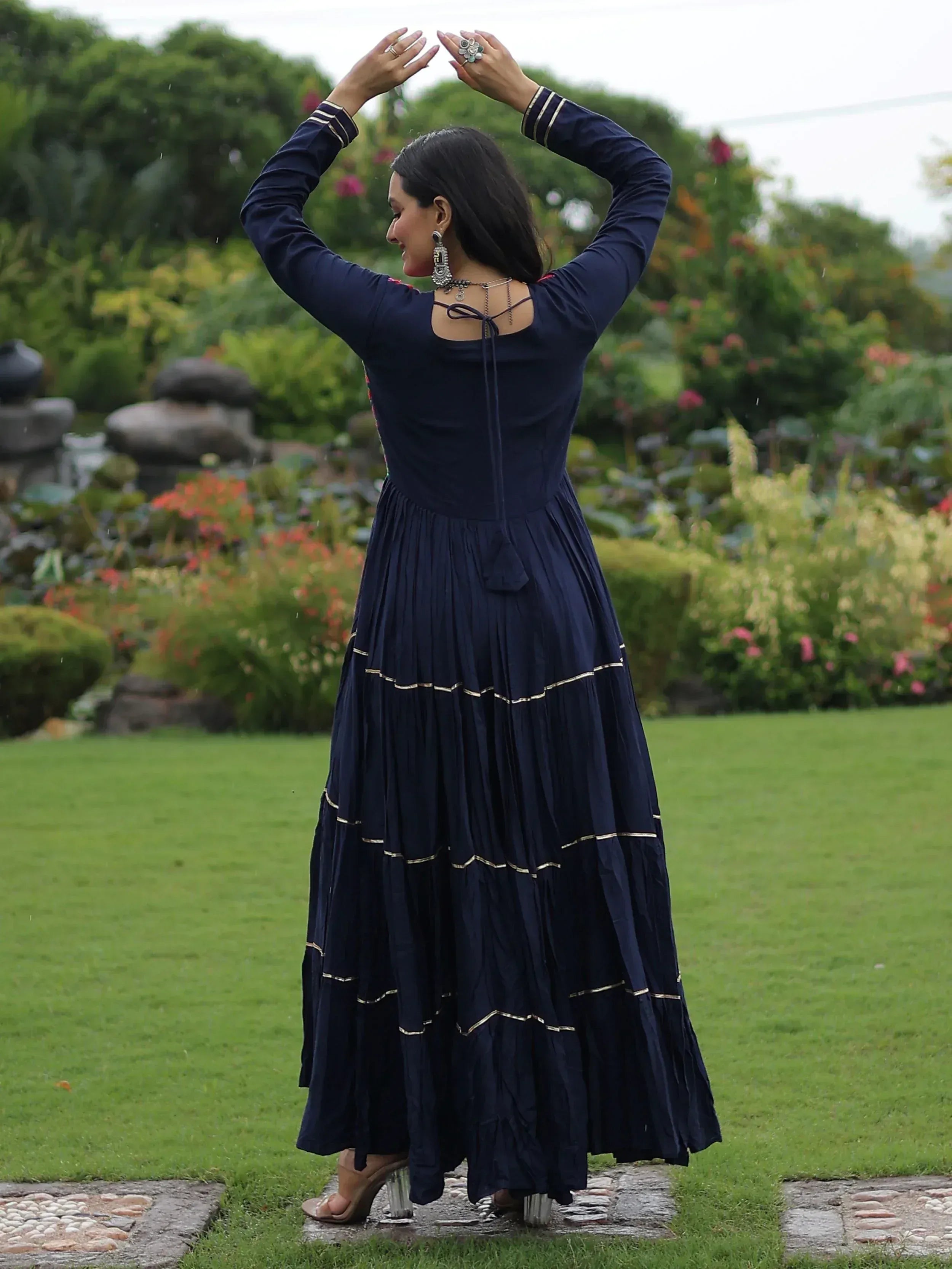 Navy blue ethnic gown with gold trim, pleated skirt, and back tie, worn in garden setting