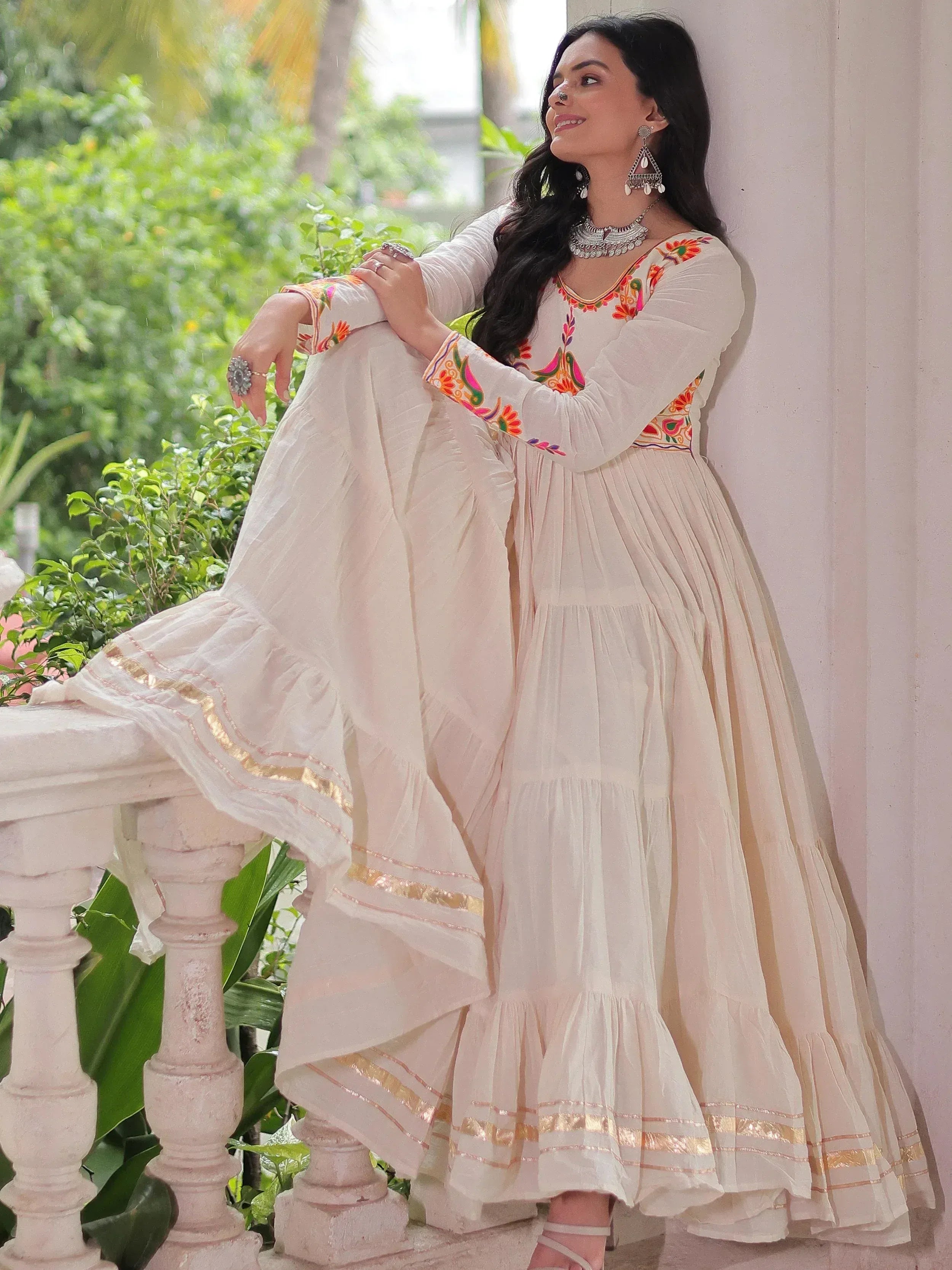 White embroidered Anarkali gown with gold trim, styled with traditional jewelry for ethnic wear