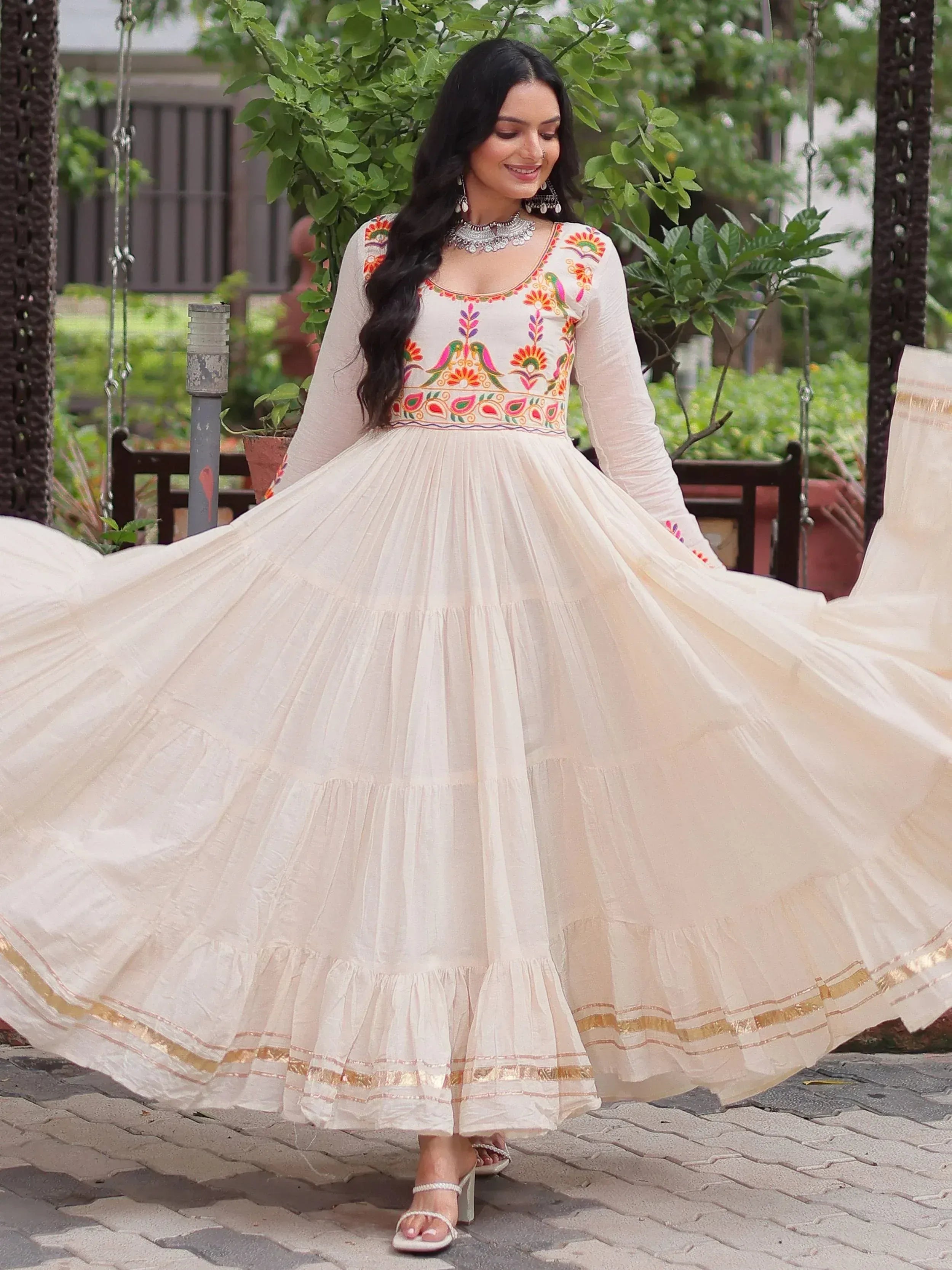 Woman in white embroidered ethnic gown with floral motifs, twirling outdoors