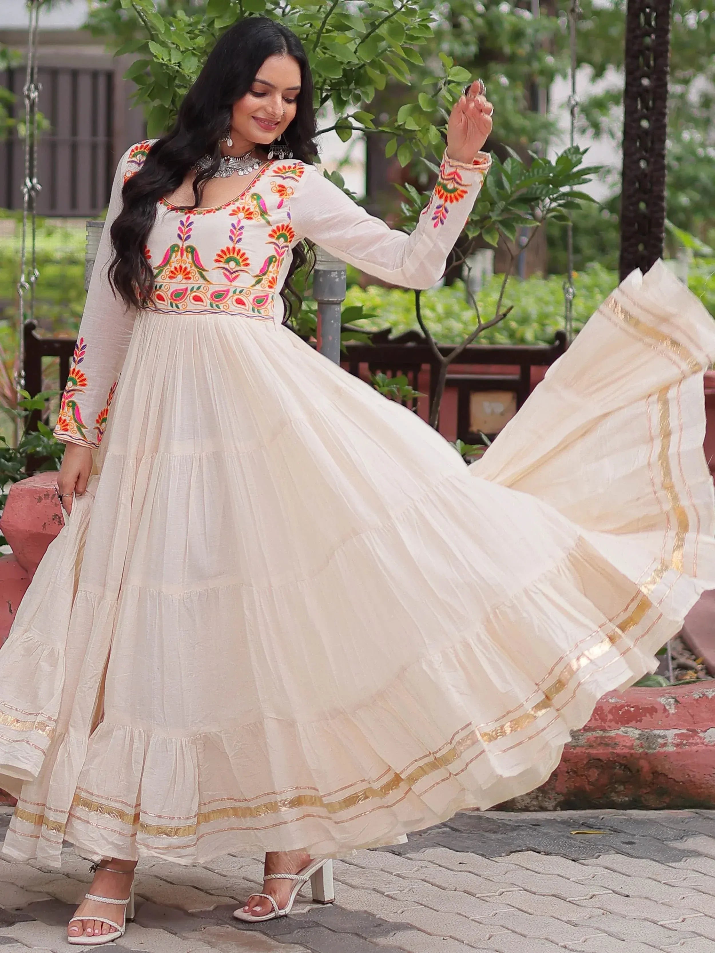 Woman in white embroidered ethnic gown with gold trim, twirling outdoors
