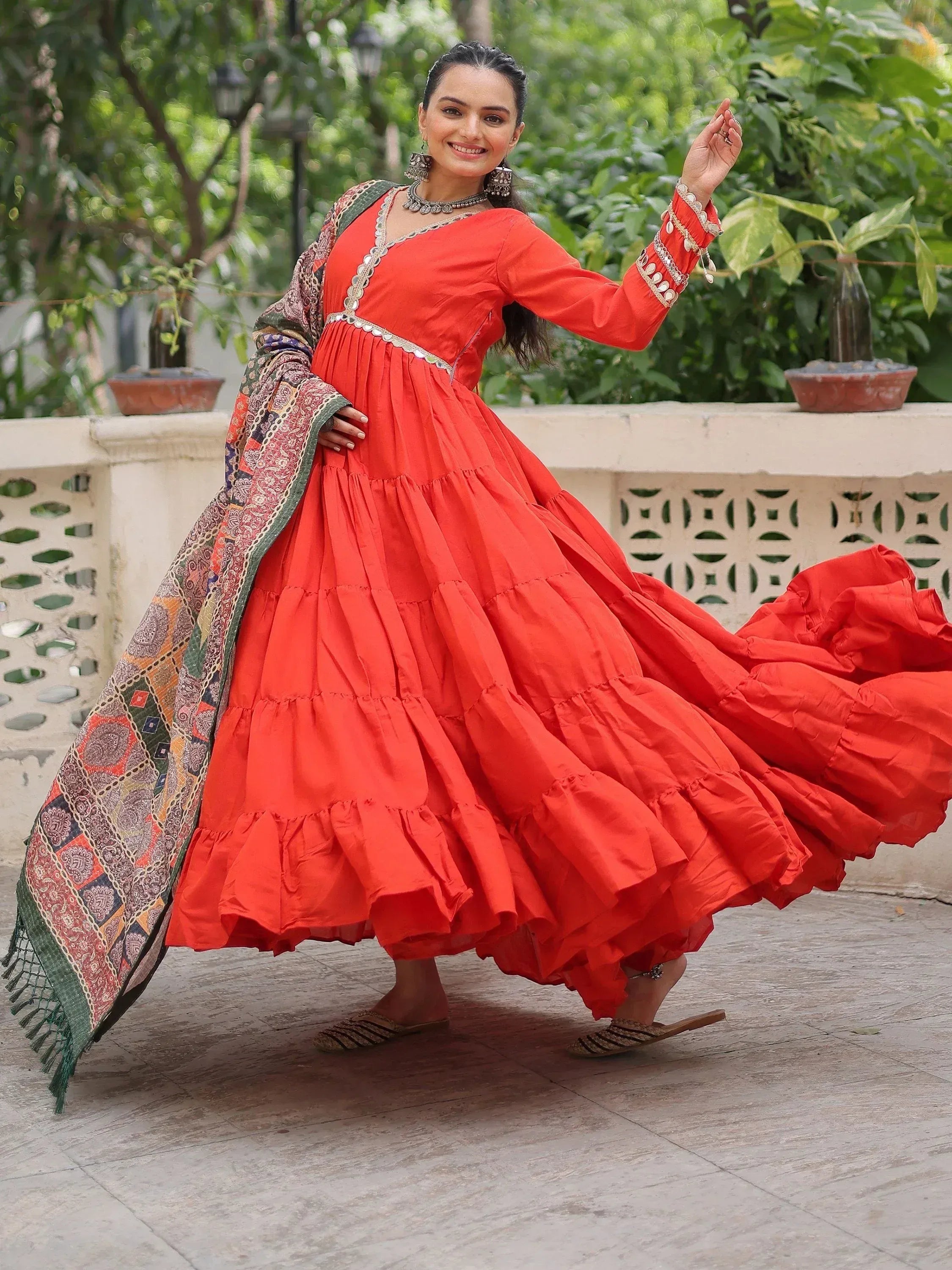 Vibrant red tiered ethnic gown with intricate embroidery and colorful dupatta, perfect for festive occasions.