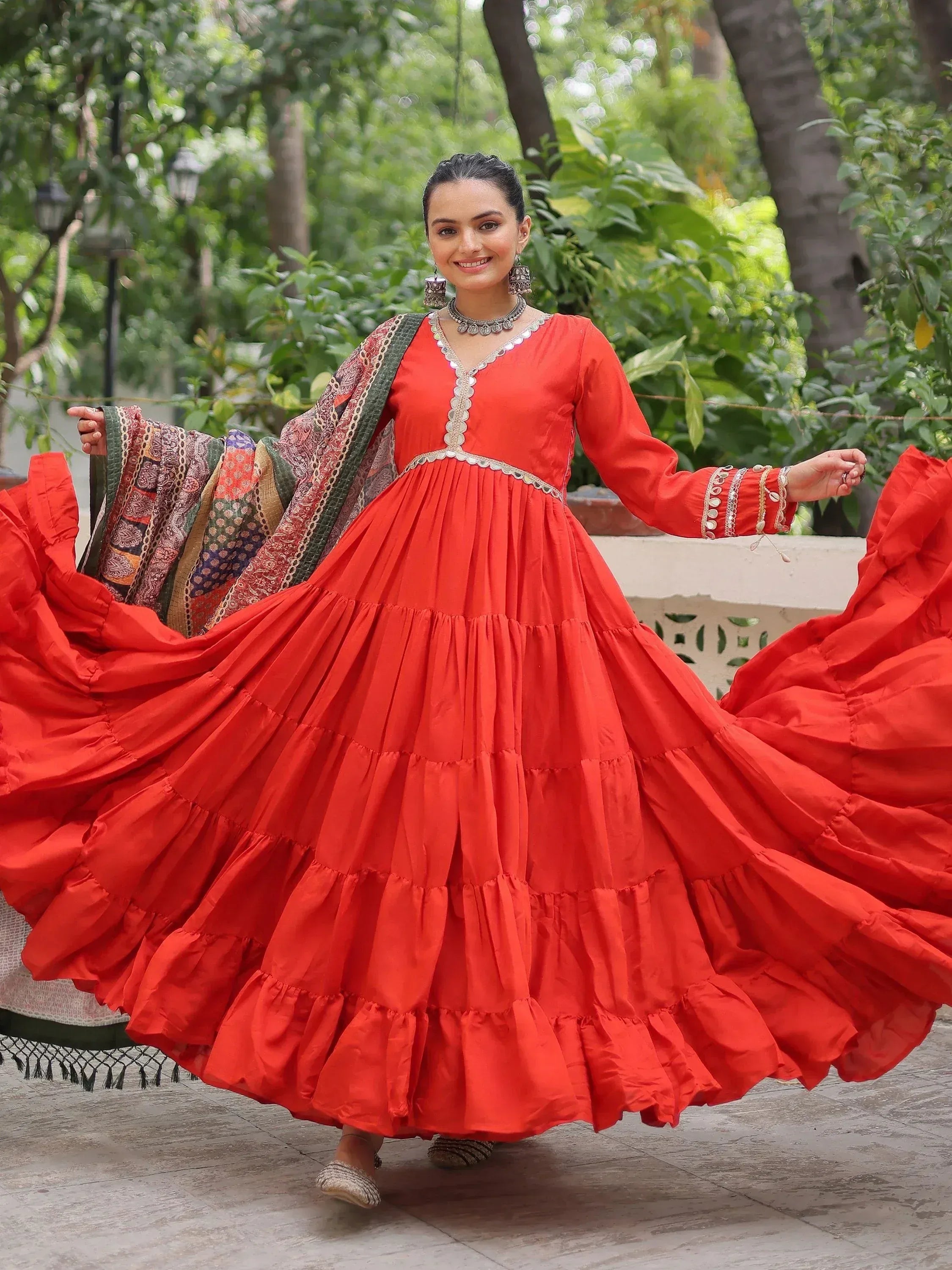 Vibrant red tiered ethnic gown with intricate embroidery and dupatta, perfect for festive occasions.