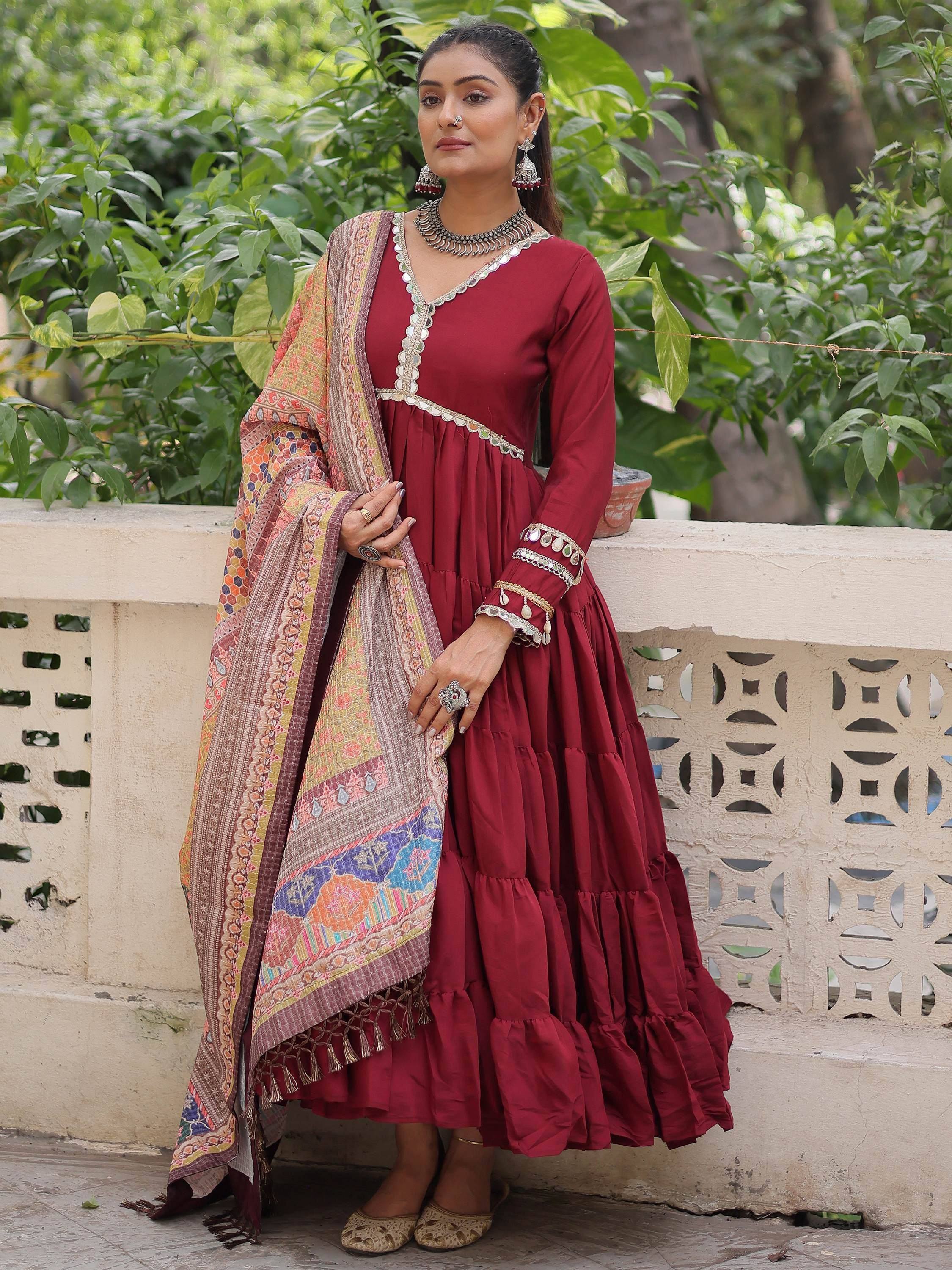 Maroon tiered ethnic gown with mirror work, paired with printed dupatta, perfect for festive occasions.