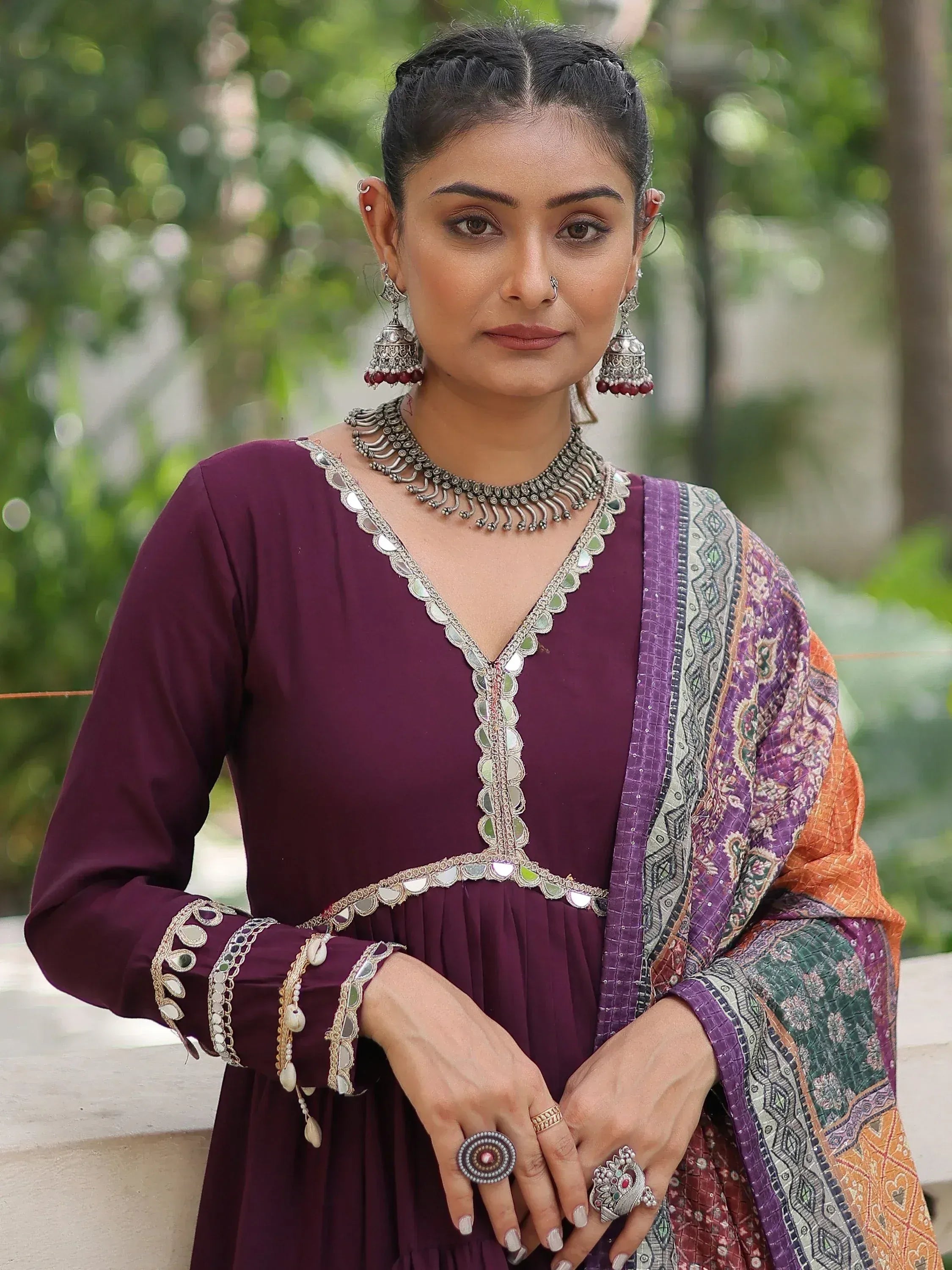 Woman in purple ethnic gown with mirror work, paired with patterned dupatta and traditional jewelry