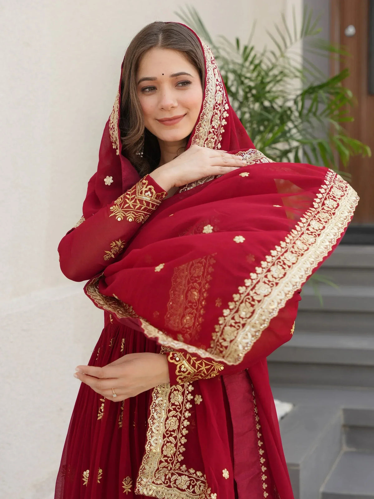 Woman in maroon ethnic gown with gold embroidery, perfect for Indian weddings or festive occasions.