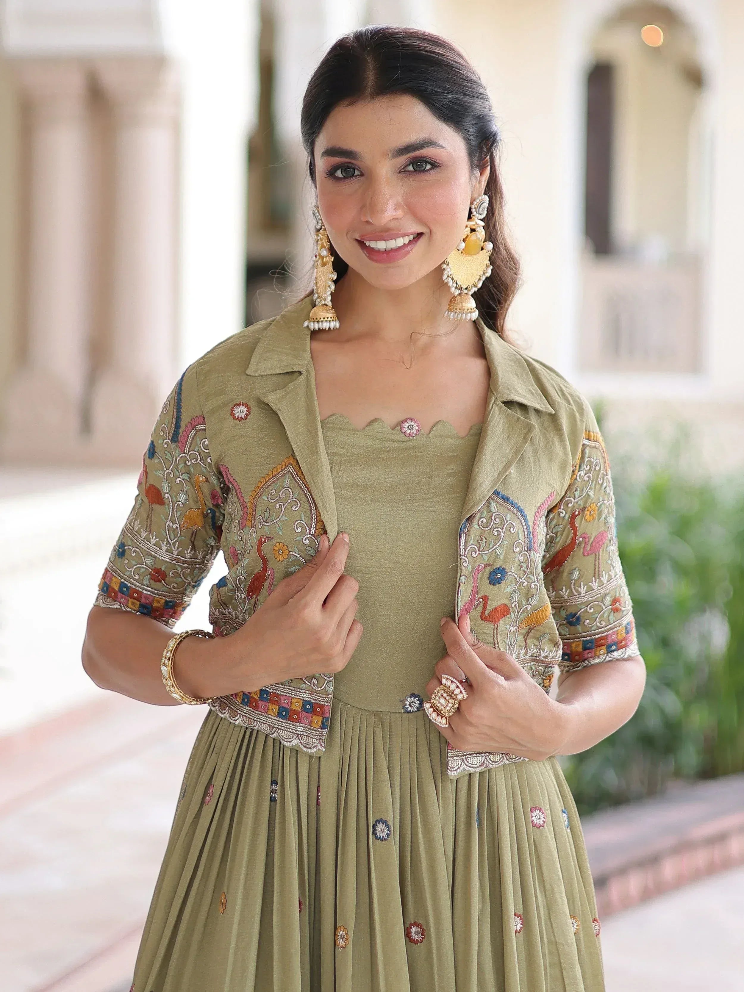 Olive green embroidered ethnic gown with floral and bird motifs, paired with statement earrings