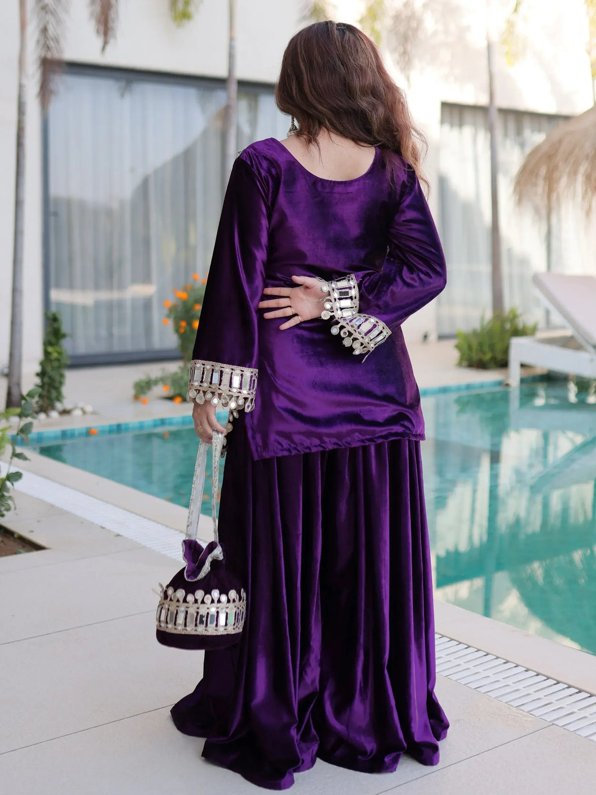 Purple velvet ethnic gown with mirror work, paired with matching bag, by poolside