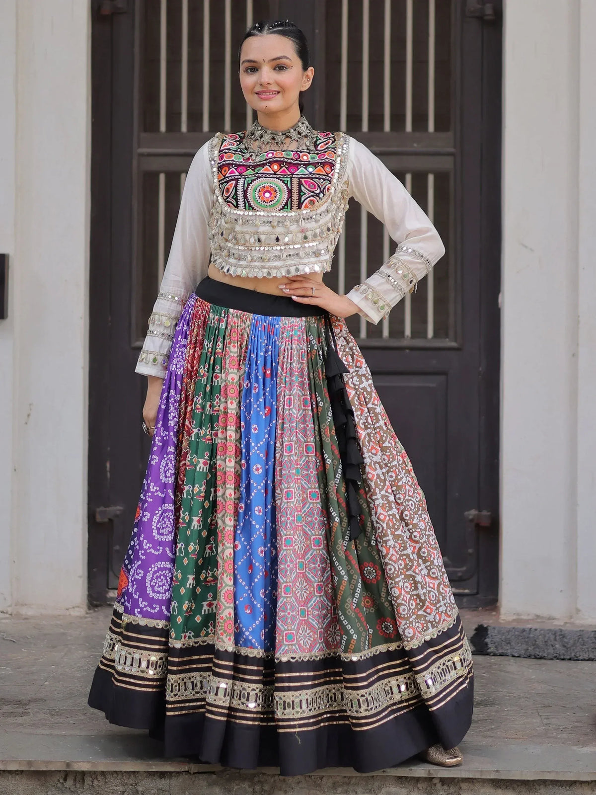 Woman in colorful embroidered Indian lehenga choli with mirror work, standing before wooden door