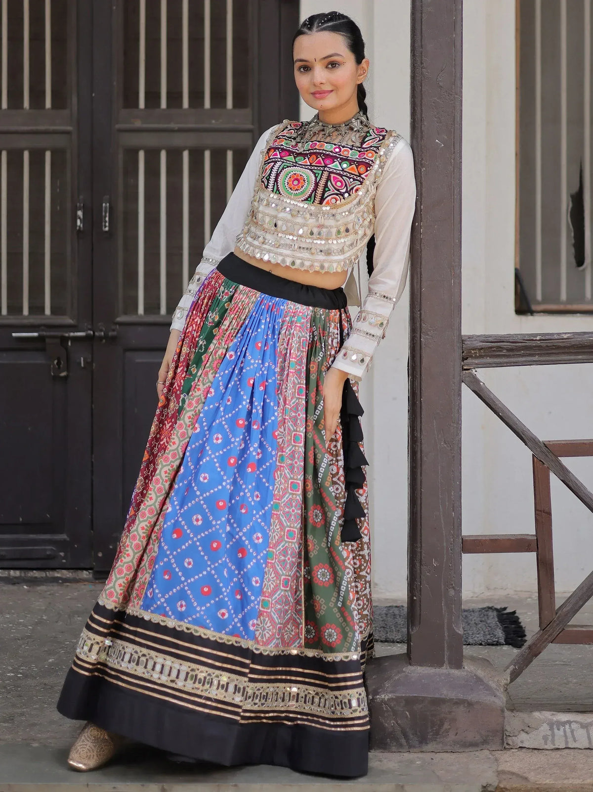 Woman in colorful embroidered Indian lehenga choli with mirror work, standing by wooden door