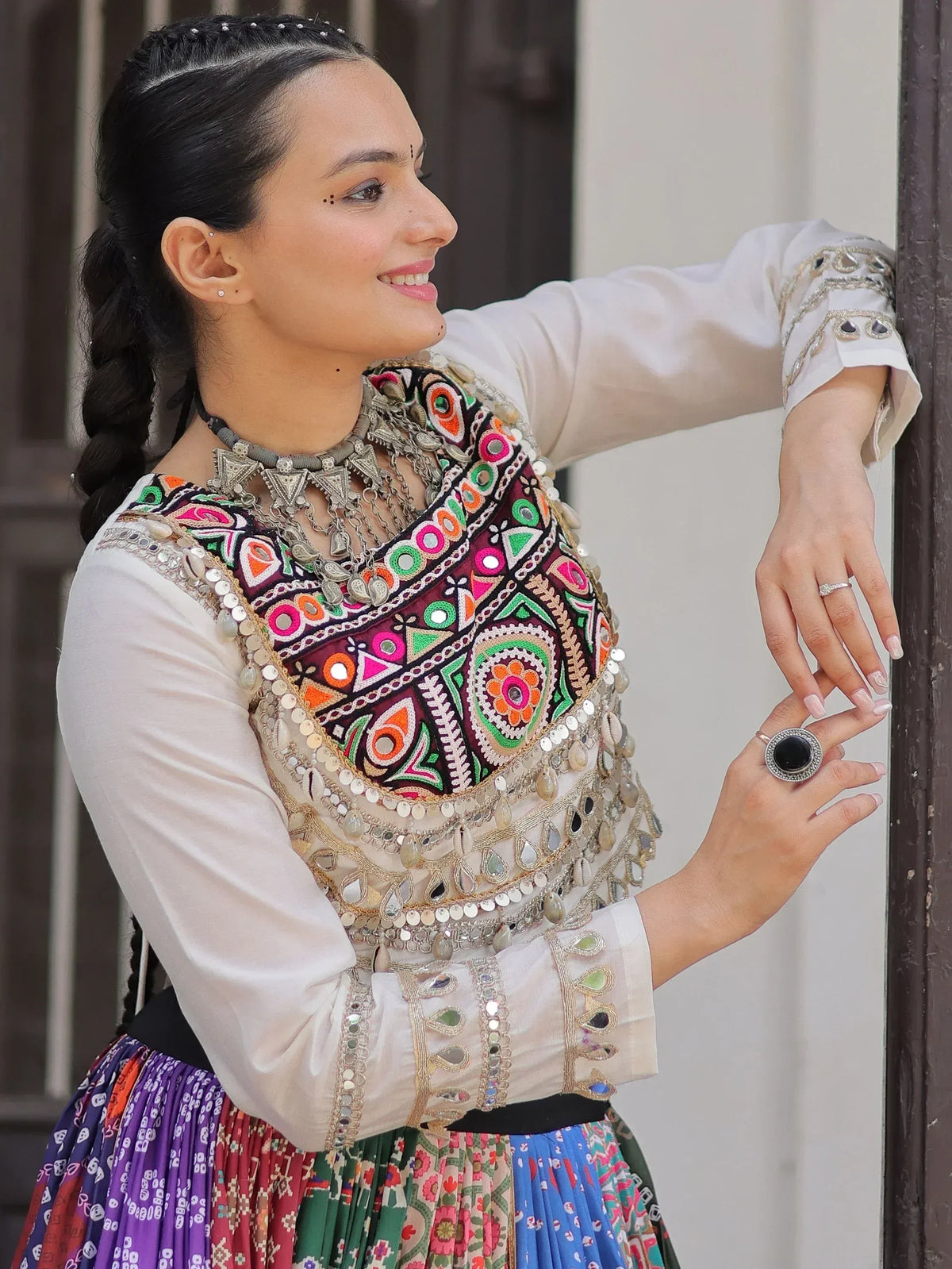 Woman in colorful embroidered ethnic wear with mirror work and traditional jewelry, perfect for festive occasions.