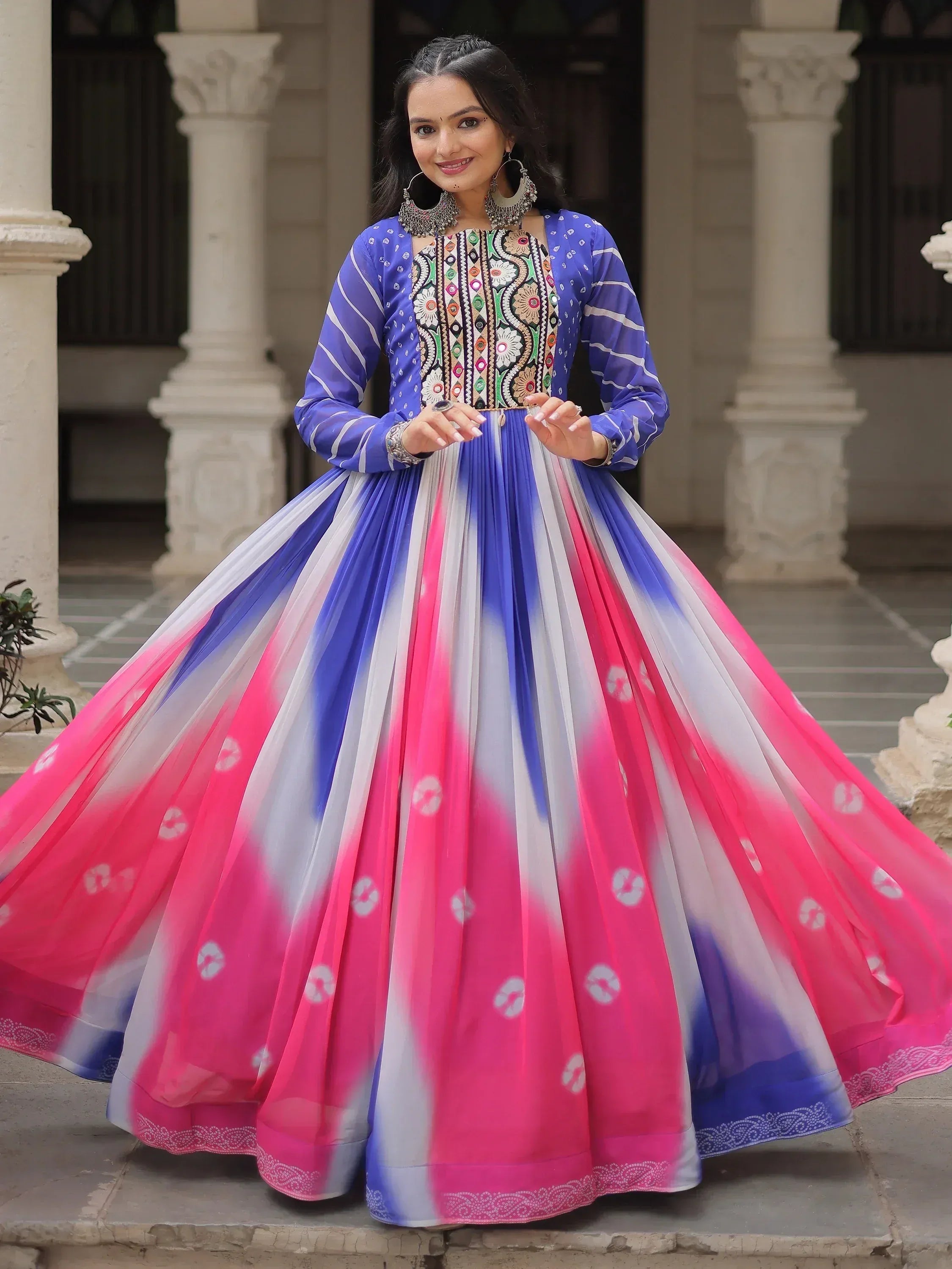 Woman in vibrant blue and pink embroidered ethnic gown with tie-dye skirt, perfect for Indian festive occasions.