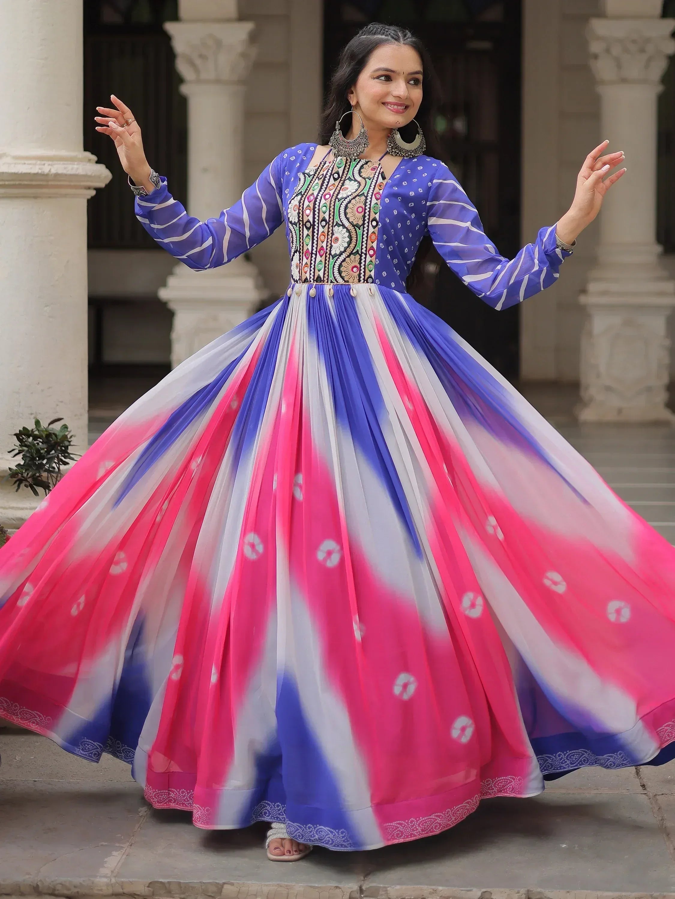 Woman in vibrant blue and pink ethnic gown with embroidered bodice, twirling outdoors