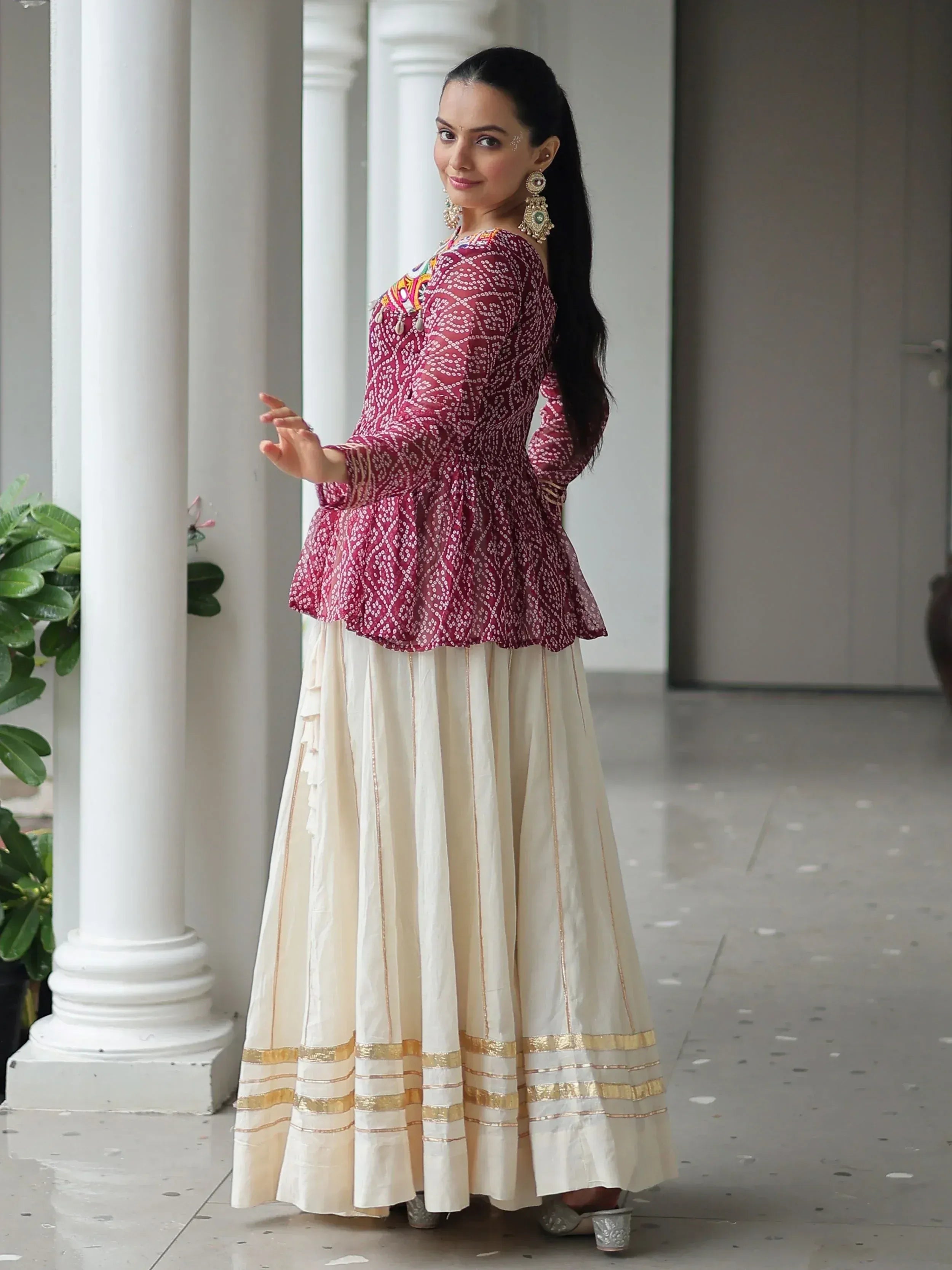 Woman in maroon printed peplum top with cream pleated skirt, ethnic Indian wear