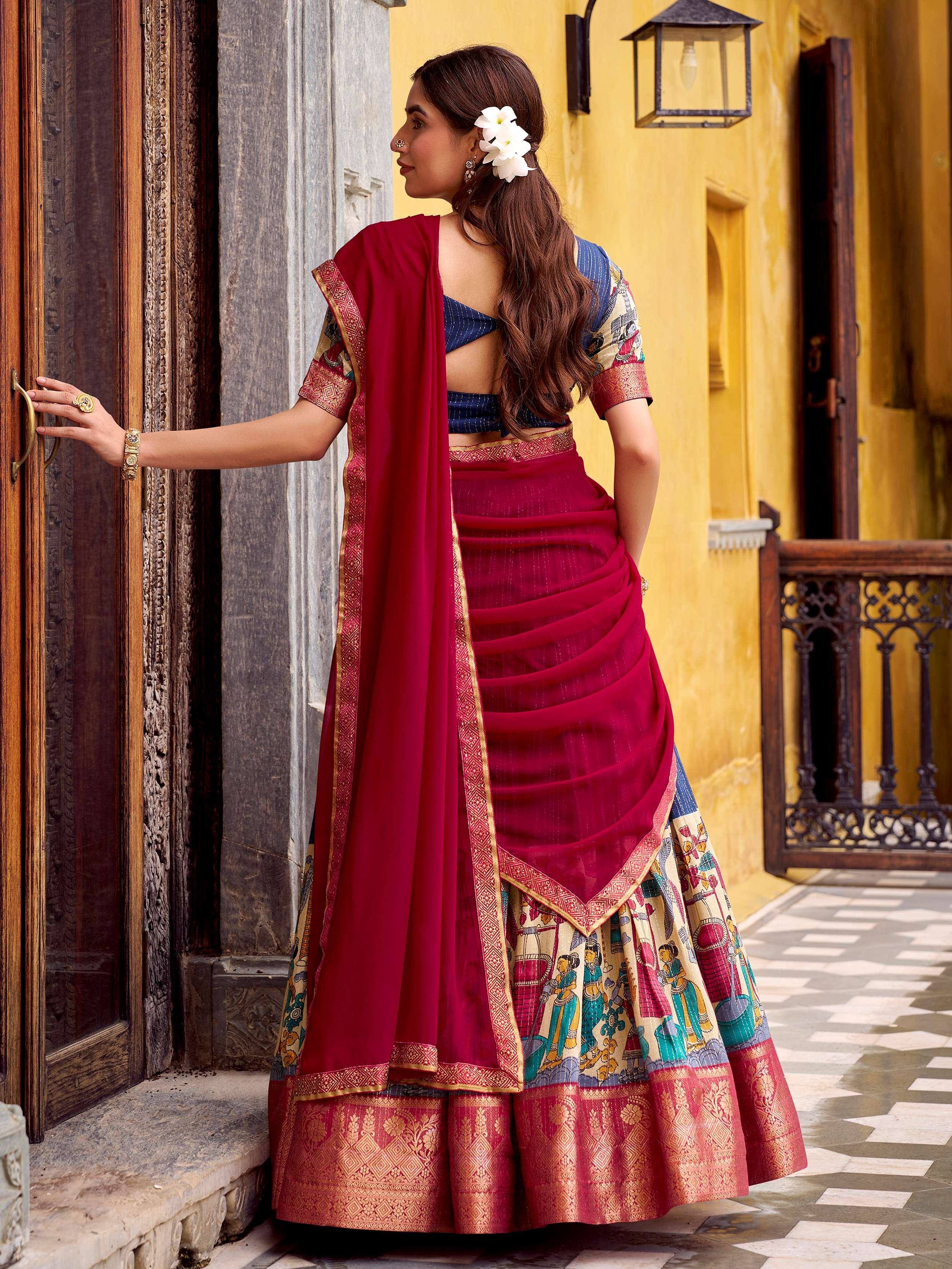 Woman in maroon lehenga choli with printed skirt, blue blouse, and gold border, standing by ornate door