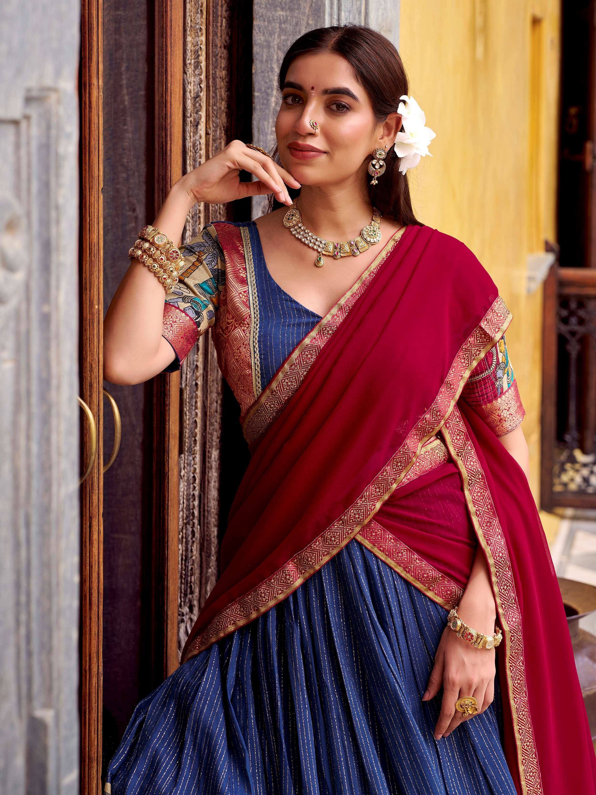 Woman in maroon and blue ethnic saree with gold border, traditional jewelry, and floral hair accessory
