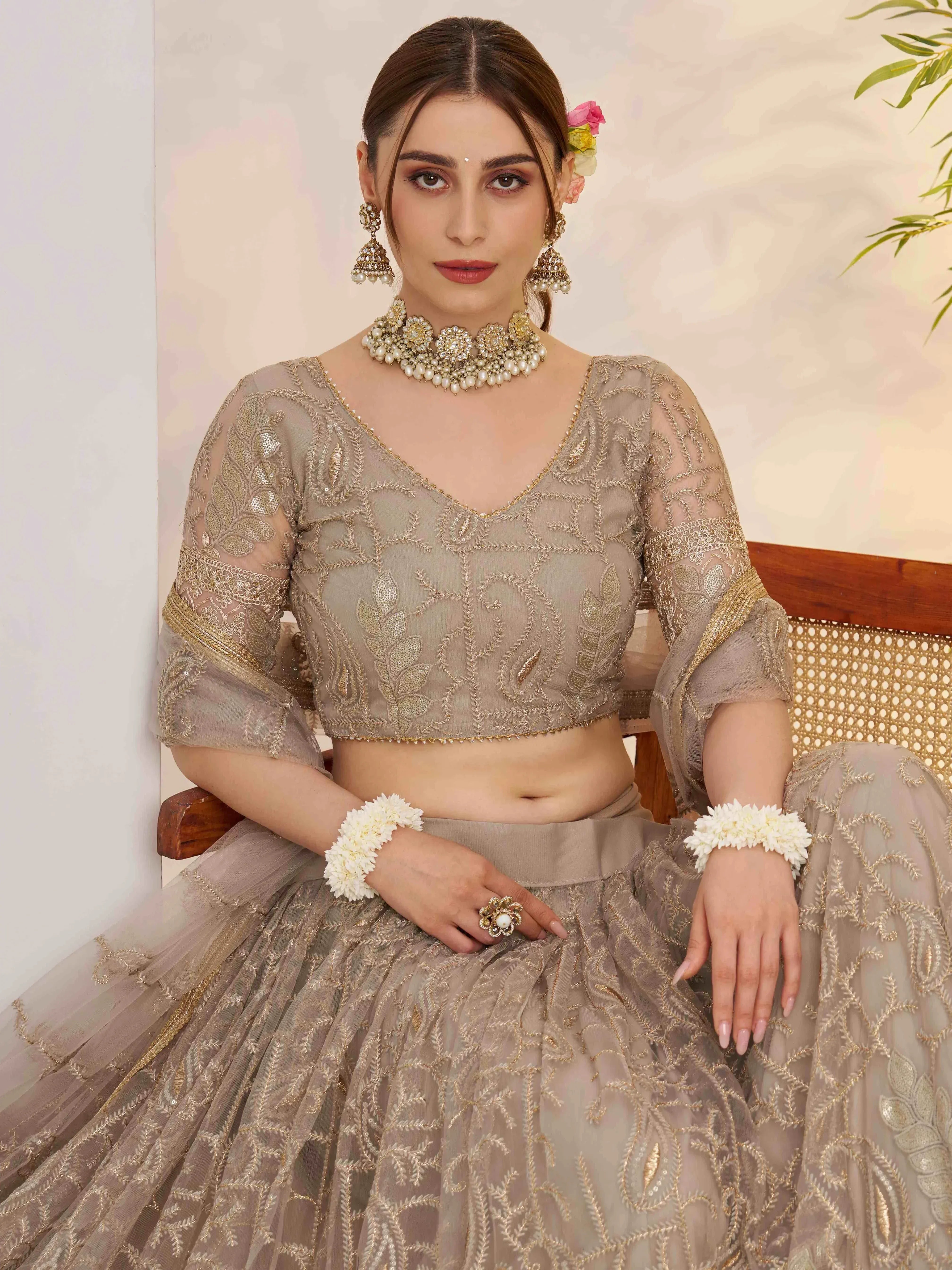 Elegant beige embroidered lehenga choli with gold detailing, floral hair accessory, and traditional jewelry.