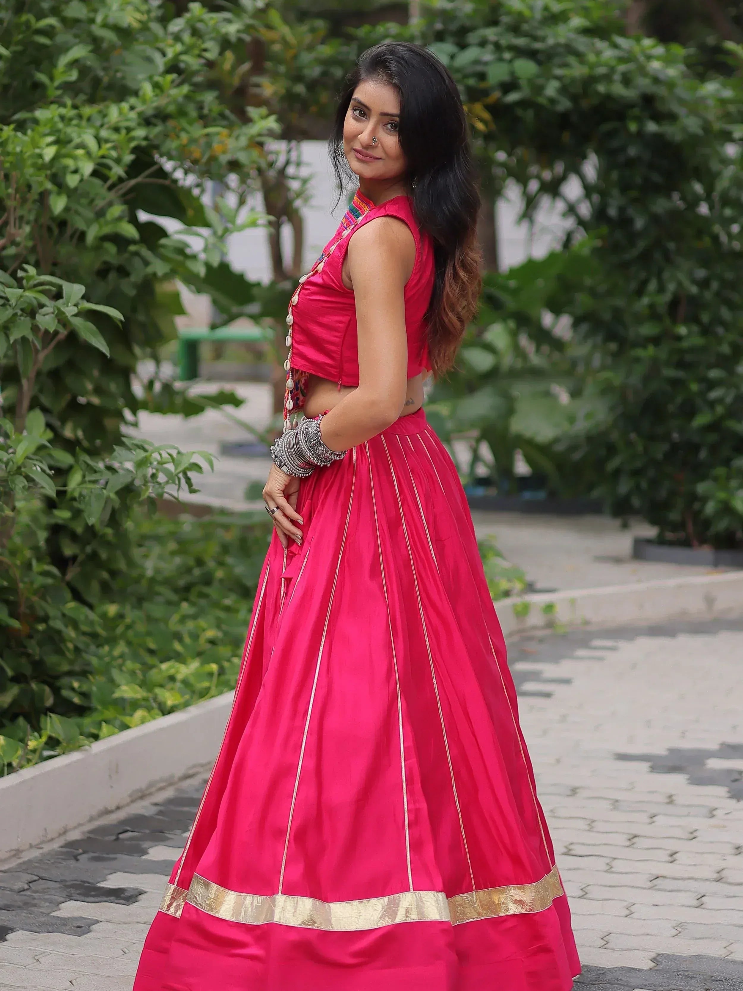 Woman in vibrant pink Indian ethnic lehenga choli with gold trim, styled with traditional jewelry outdoors