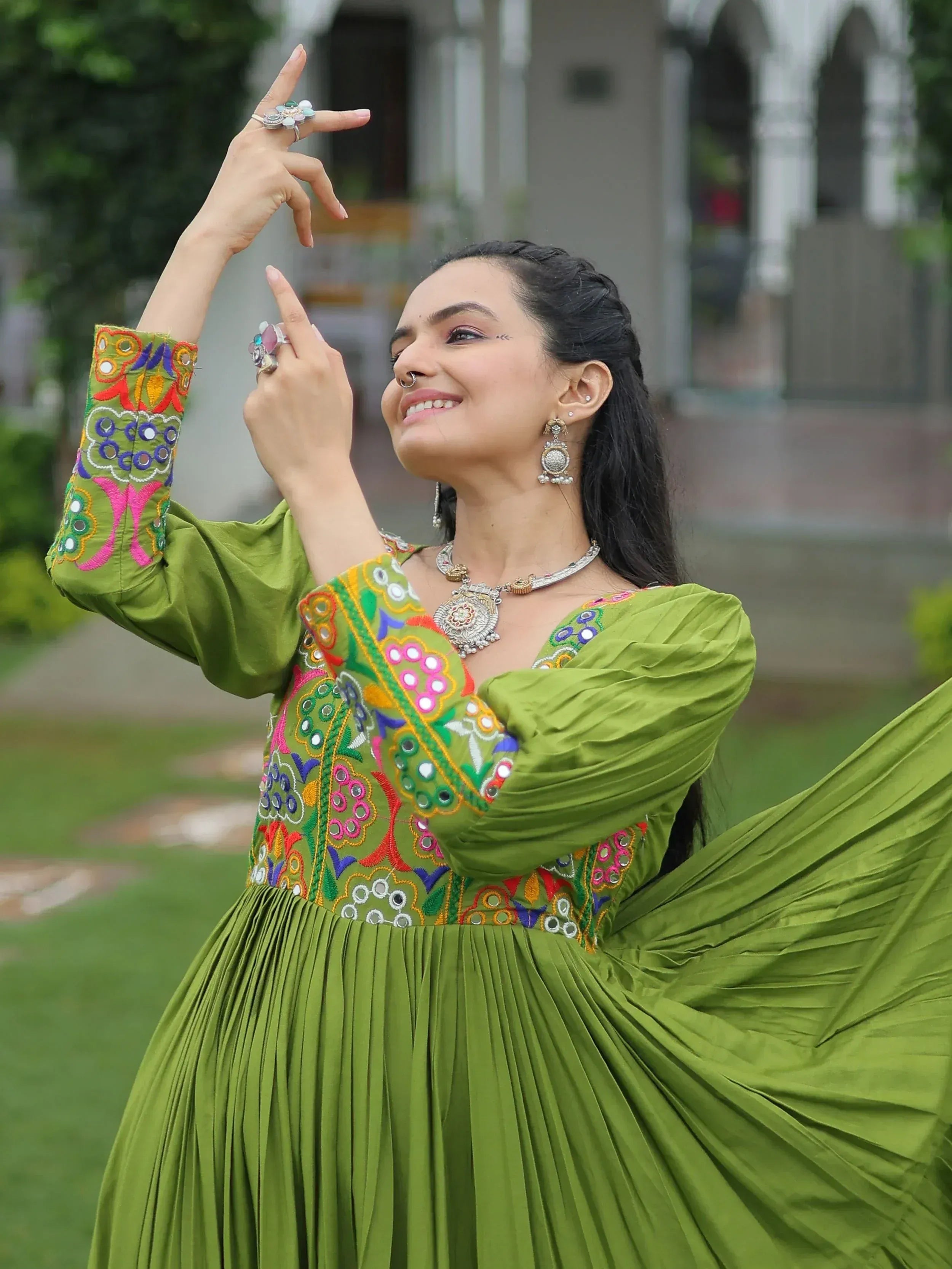 Woman in vibrant green embroidered ethnic gown with mirror work, dancing outdoors
