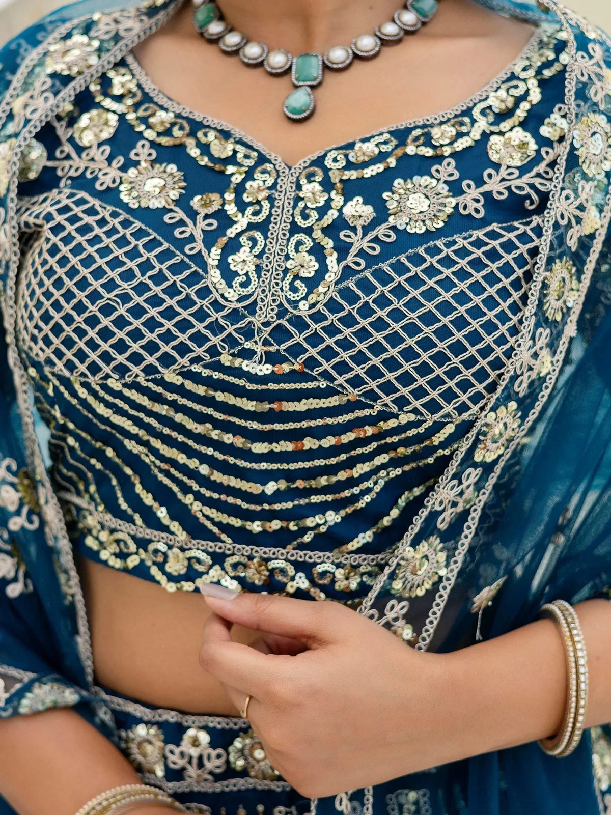 Blue embroidered lehenga choli with gold sequin work and floral detailing, paired with green stone necklace