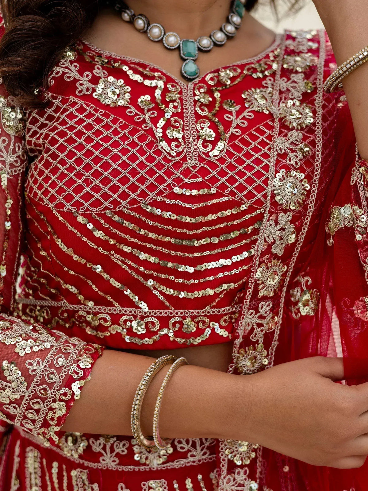 Red ethnic lehenga choli with gold sequin embroidery and pearl necklace, perfect for Indian weddings and festive occasions.