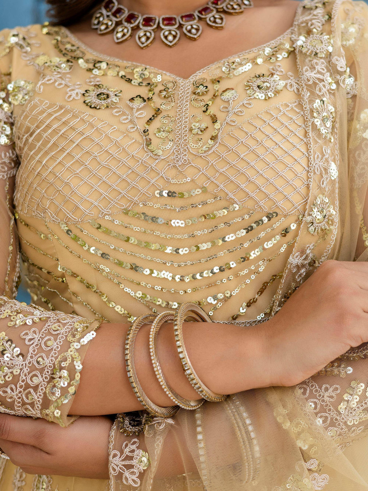 Gold sequin embroidered ethnic gown with intricate neckline and sleeve detailing, paired with statement jewelry.