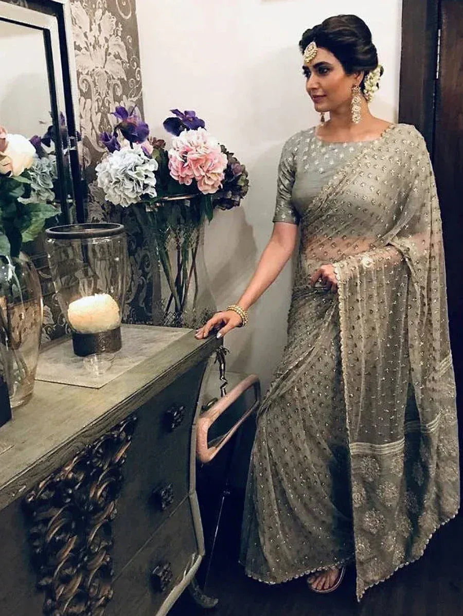 Elegant woman in embellished grey saree with floral backdrop, perfect for Indian ethnic occasions