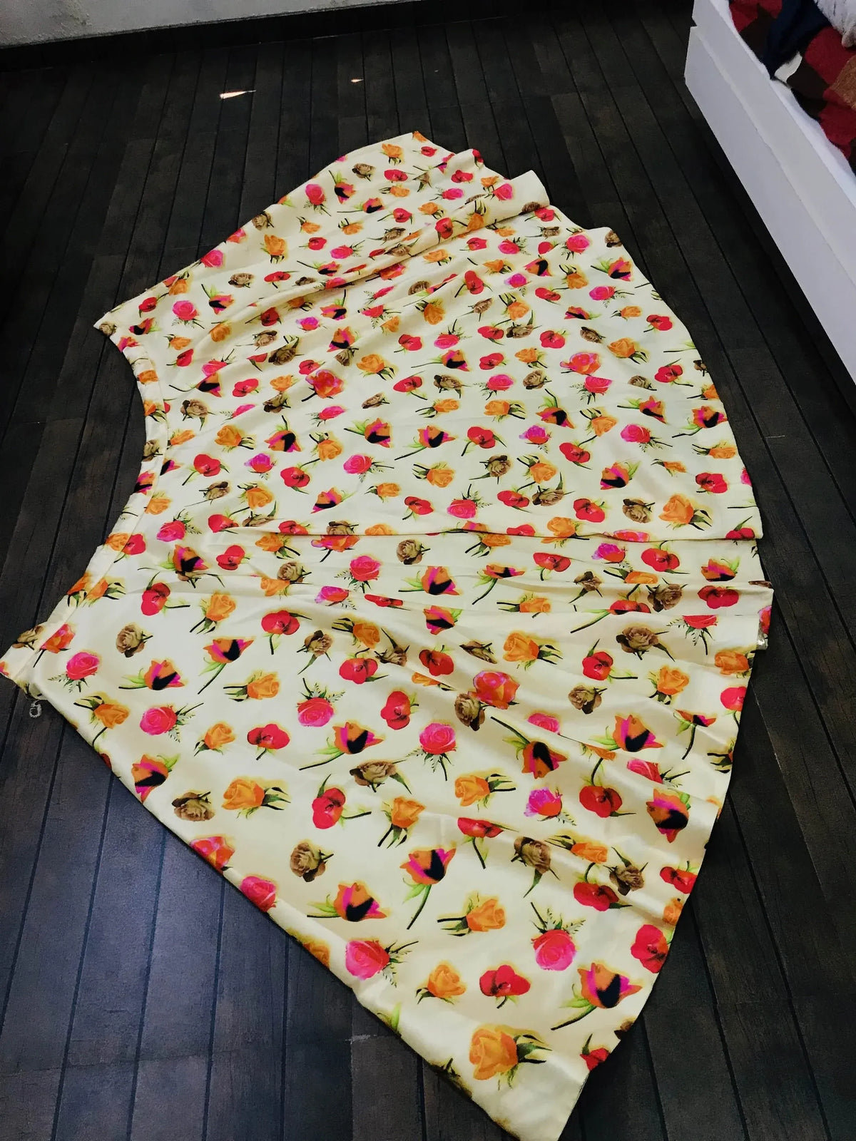 Floral print ethnic gown with pink, orange, and red roses on cream fabric, laid flat on dark wood floor