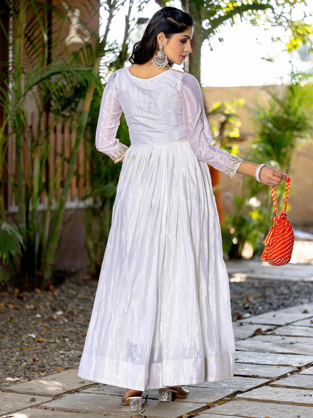 White ethnic gown with gold embroidery, pleated skirt, and orange drawstring bag for festive occasions