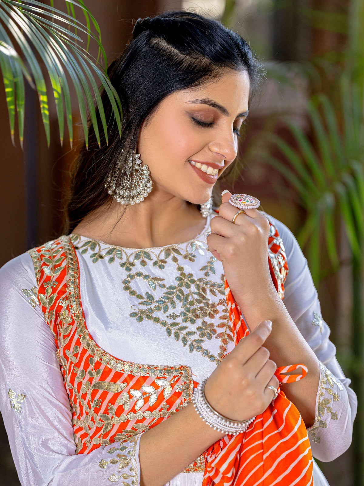 Woman in white and orange embroidered ethnic wear with mirror work, pearl jewelry, and traditional Indian accessories