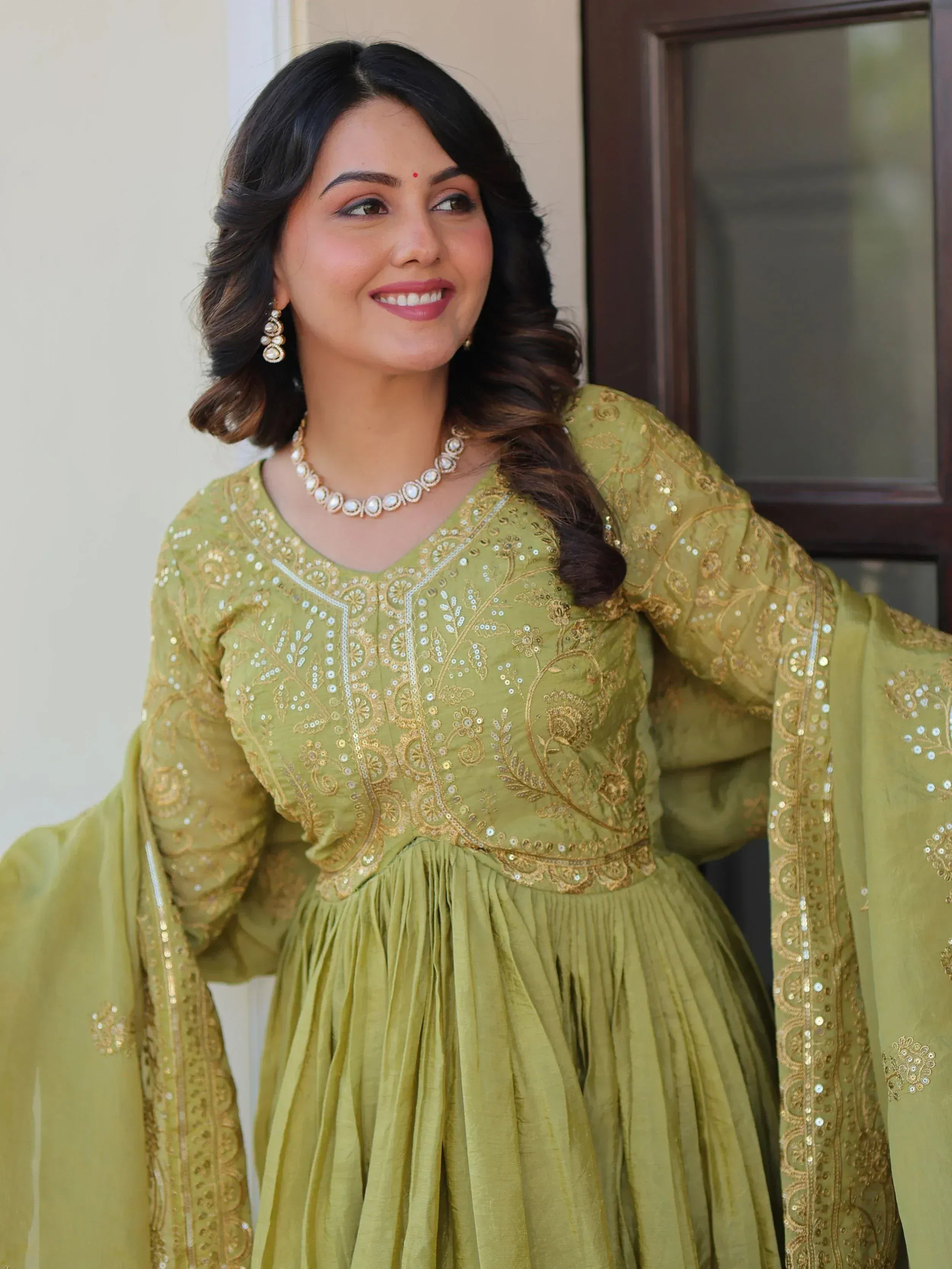 Woman in olive green embroidered ethnic gown with gold detailing and pearl jewelry