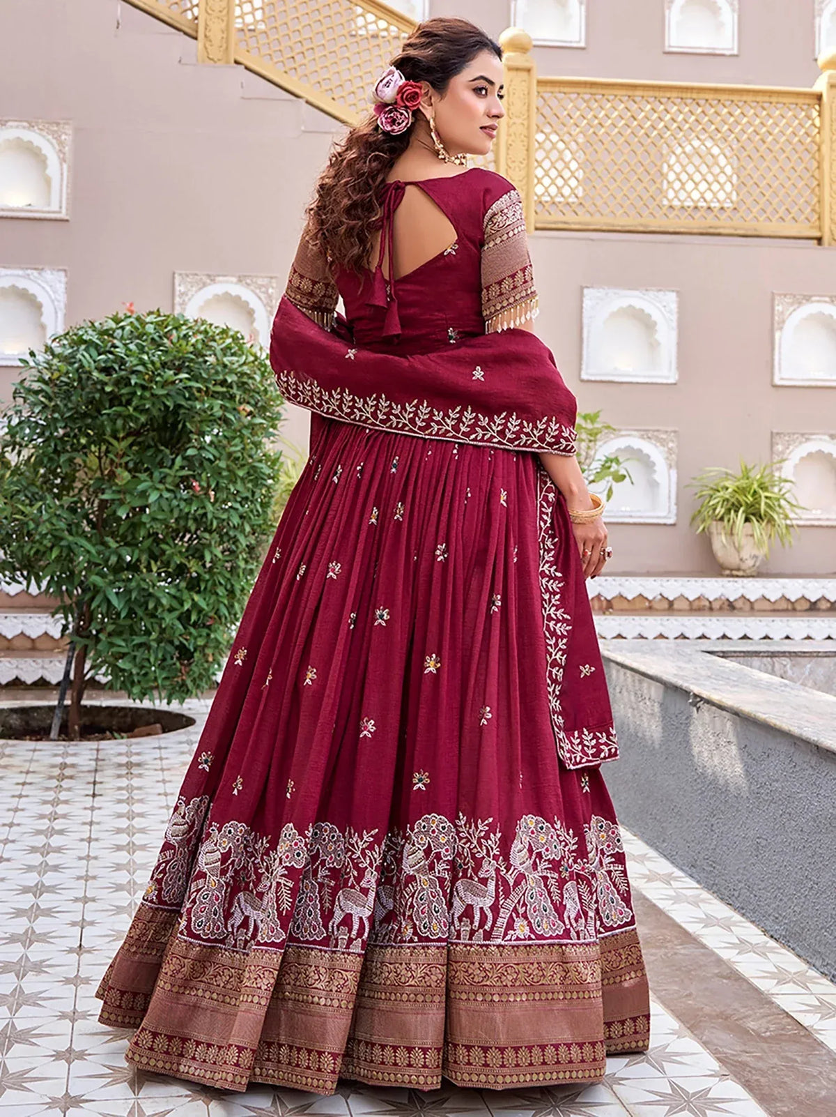Woman in a maroon designer lehenga choli with intricate gold embroidery and ethnic patterns.